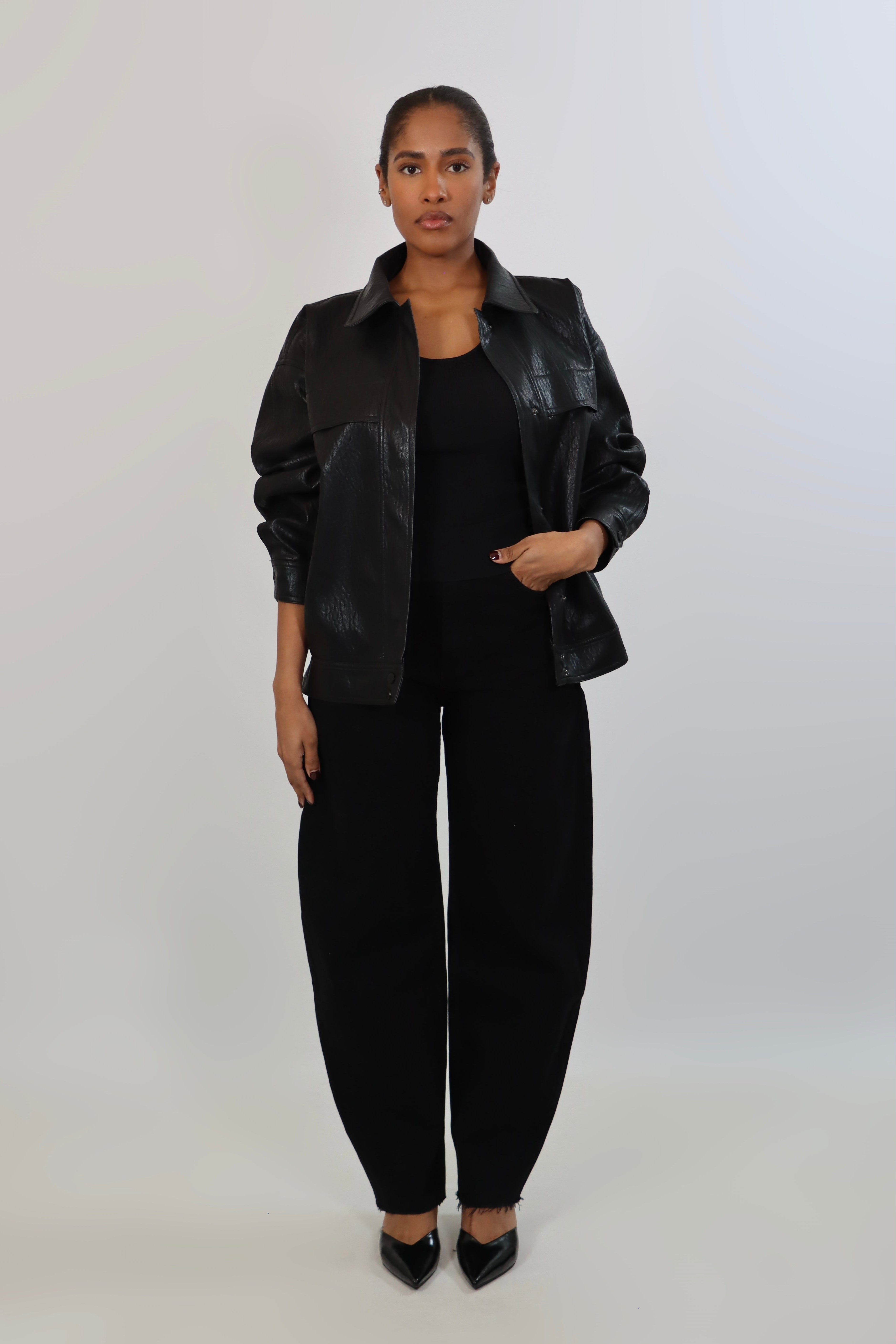 Model wearing a black textured leather oversized jacket with a structured collar and long sleeves, styled with black pants against a neutral background.