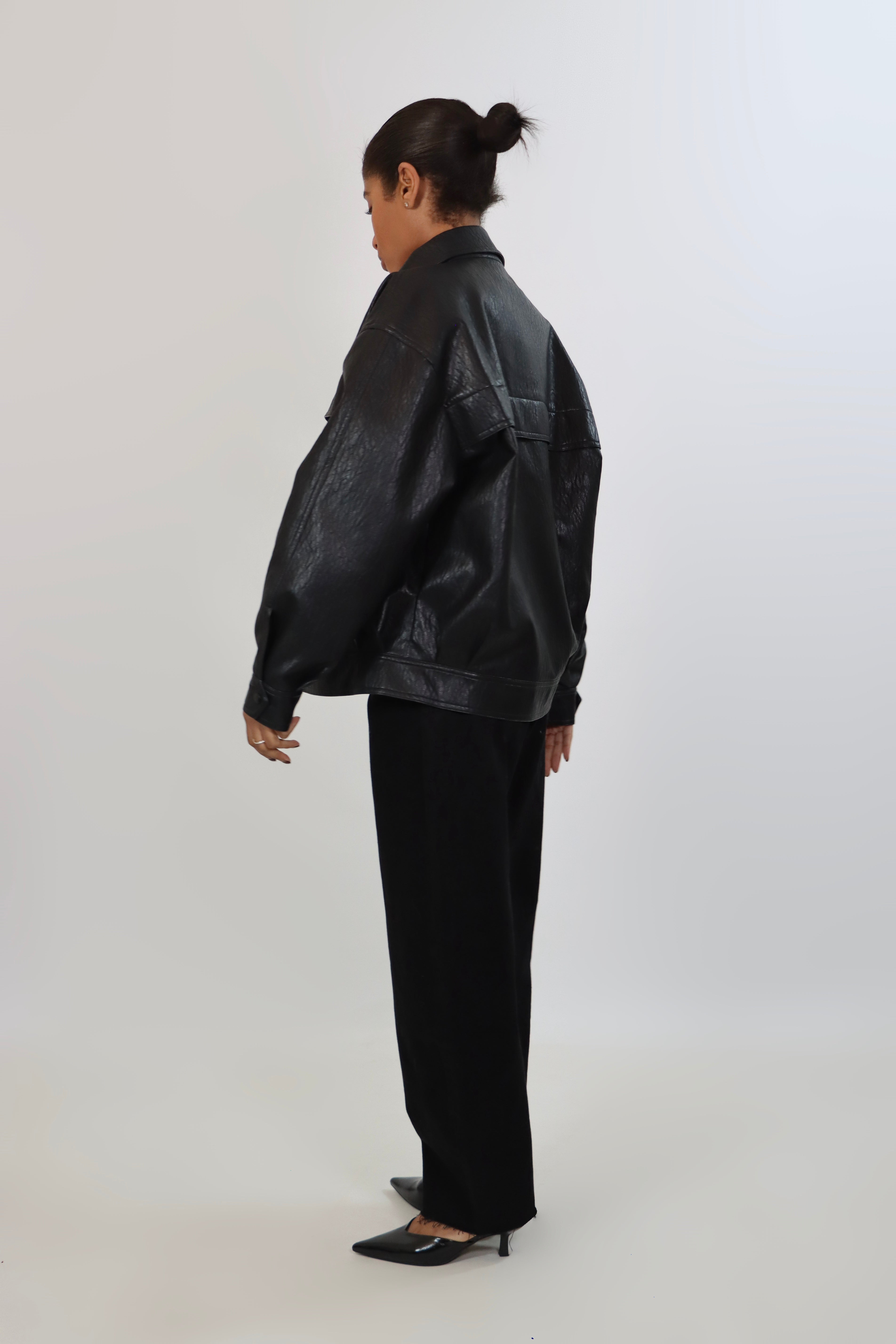 Model wearing a black textured leather oversized jacket with a structured collar and long sleeves, styled with black pants against a neutral background.