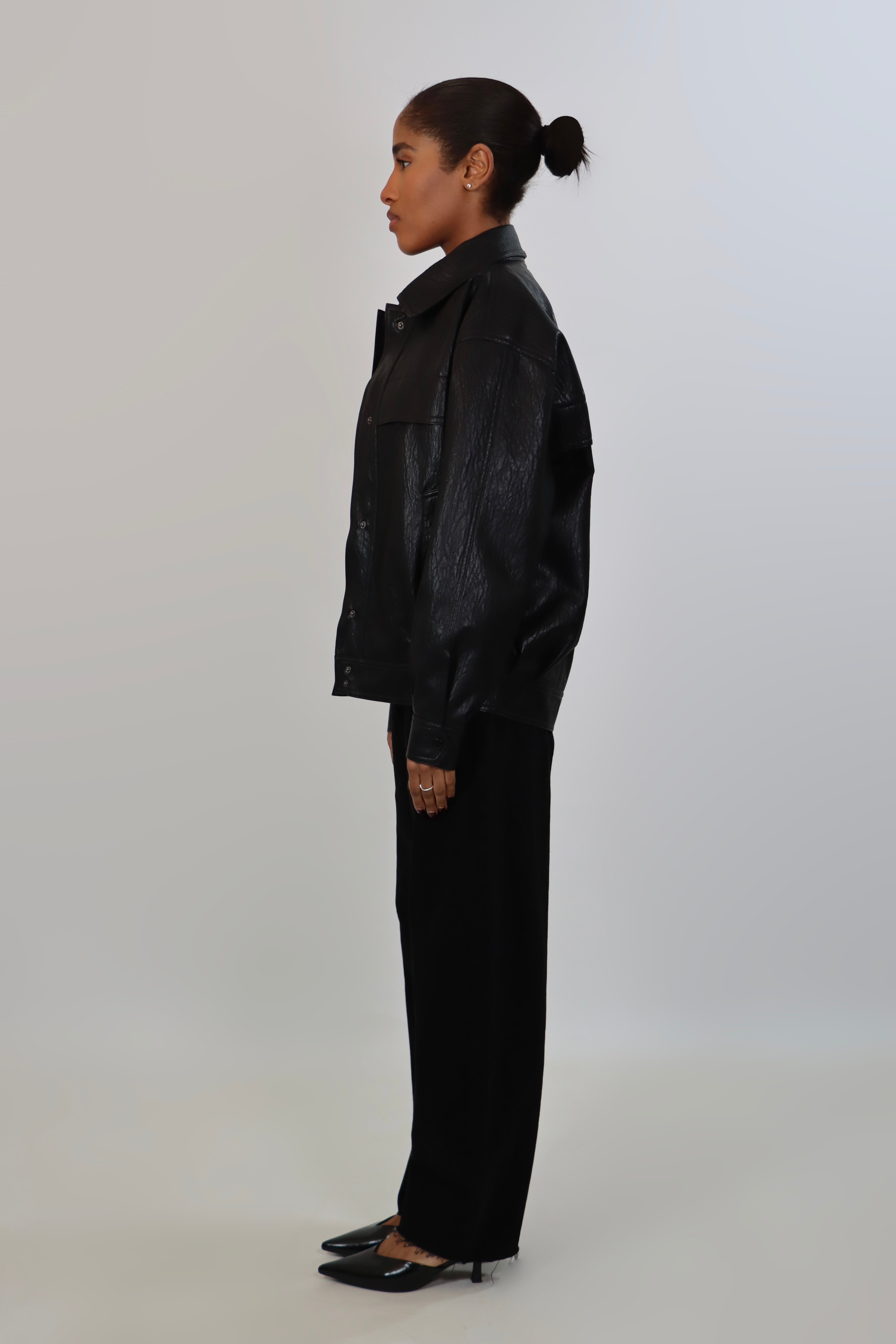 Model wearing a black textured leather oversized jacket with a structured collar and long sleeves, styled with black pants against a neutral background.
