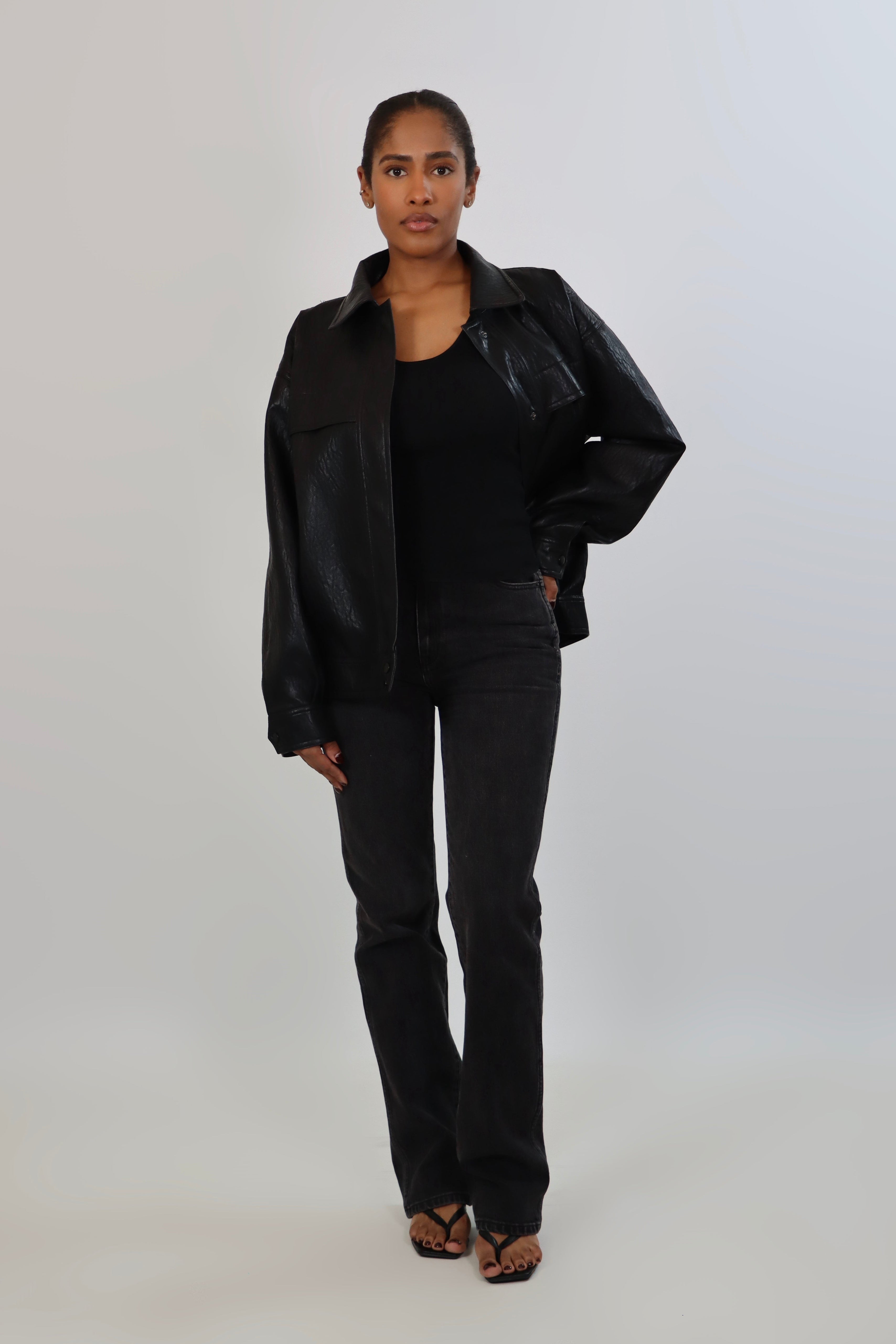 Model wearing a black textured leather oversized jacket with a structured collar and long sleeves, styled with black pants against a neutral background.