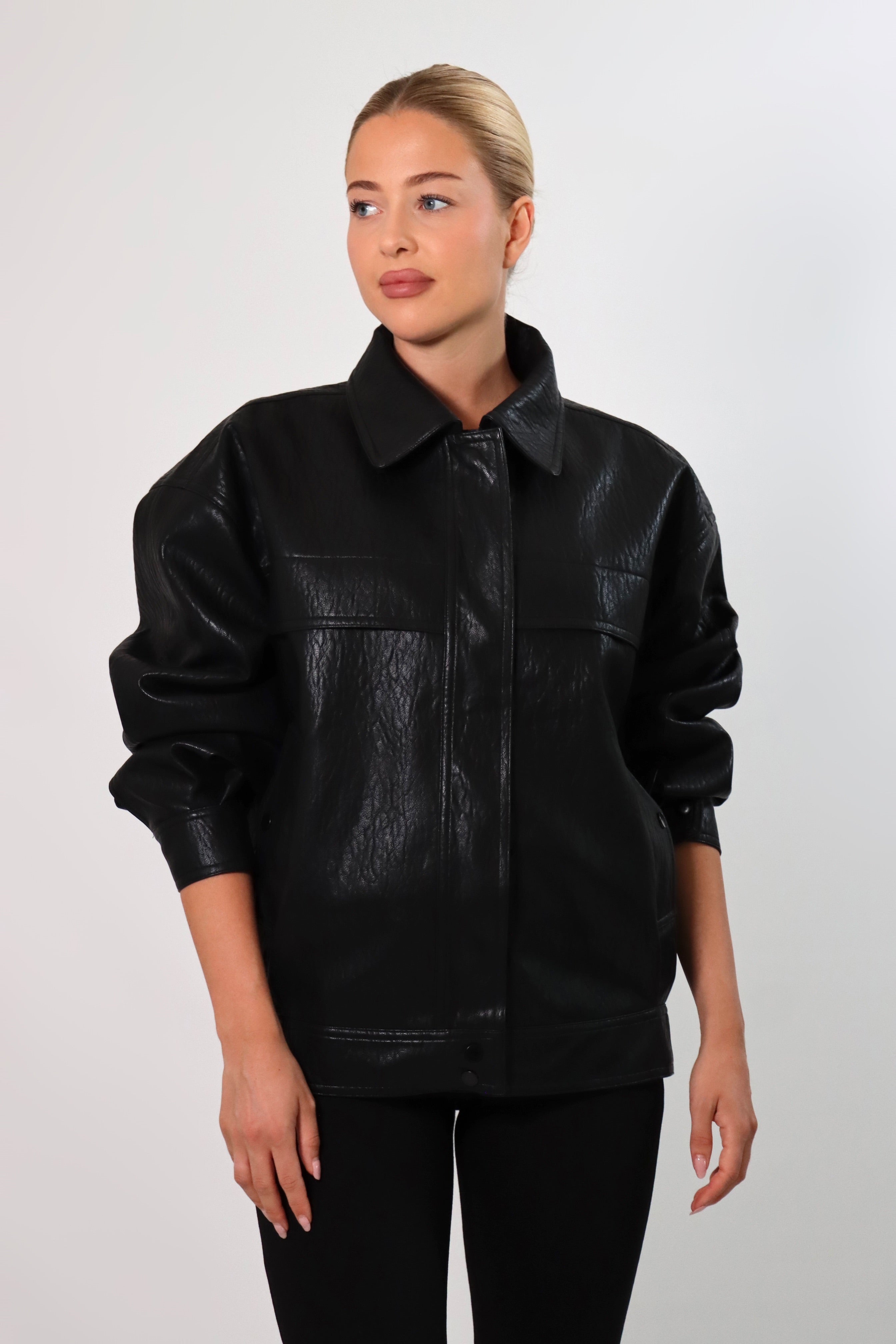 Model wearing a black textured leather oversized jacket with a structured collar and long sleeves, styled with black pants against a neutral background.