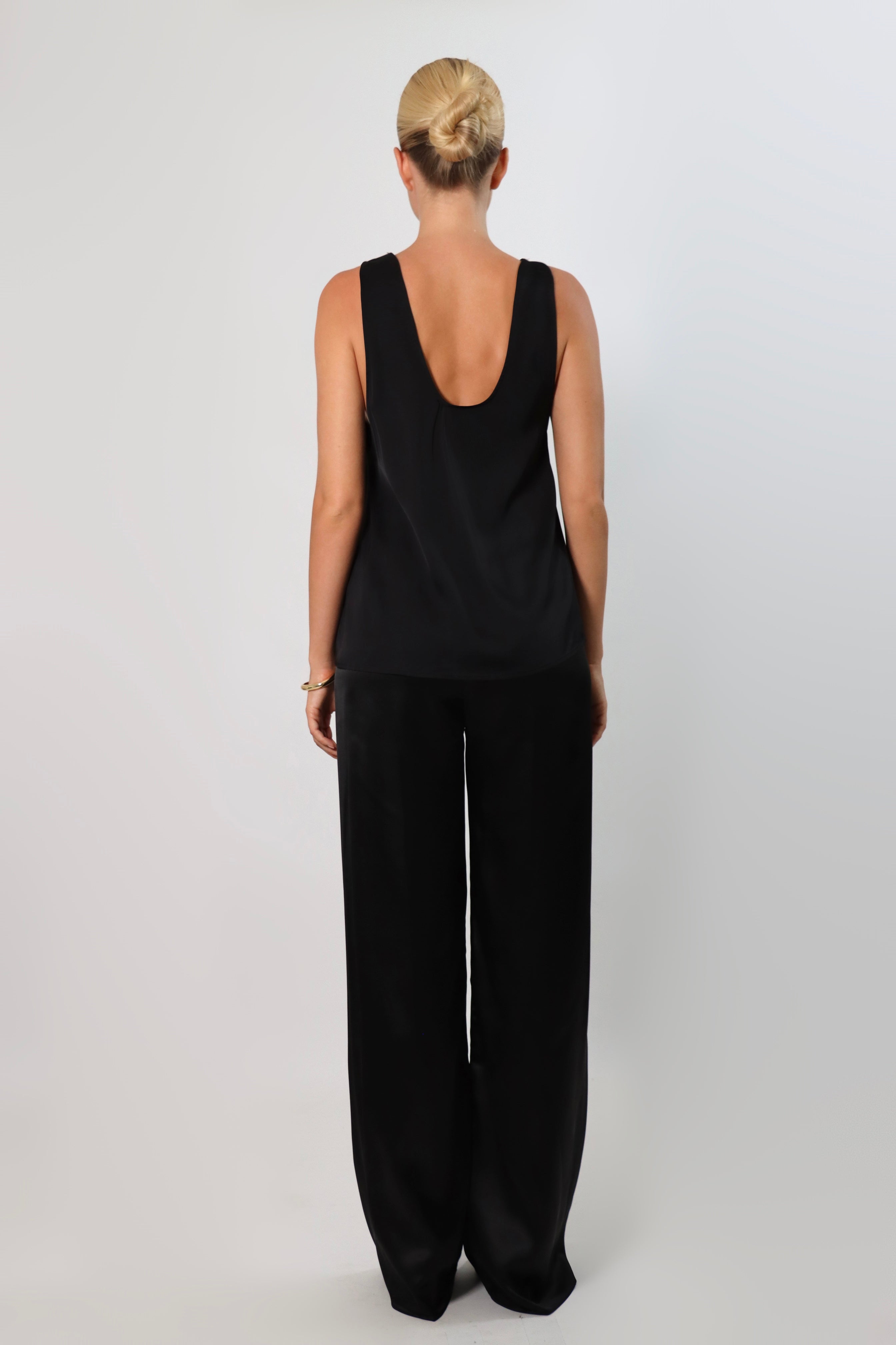 Black: Model wearing a black satin sleeveless top with a deep plunging neckline and matching satin pants for a sleek monochrome look.