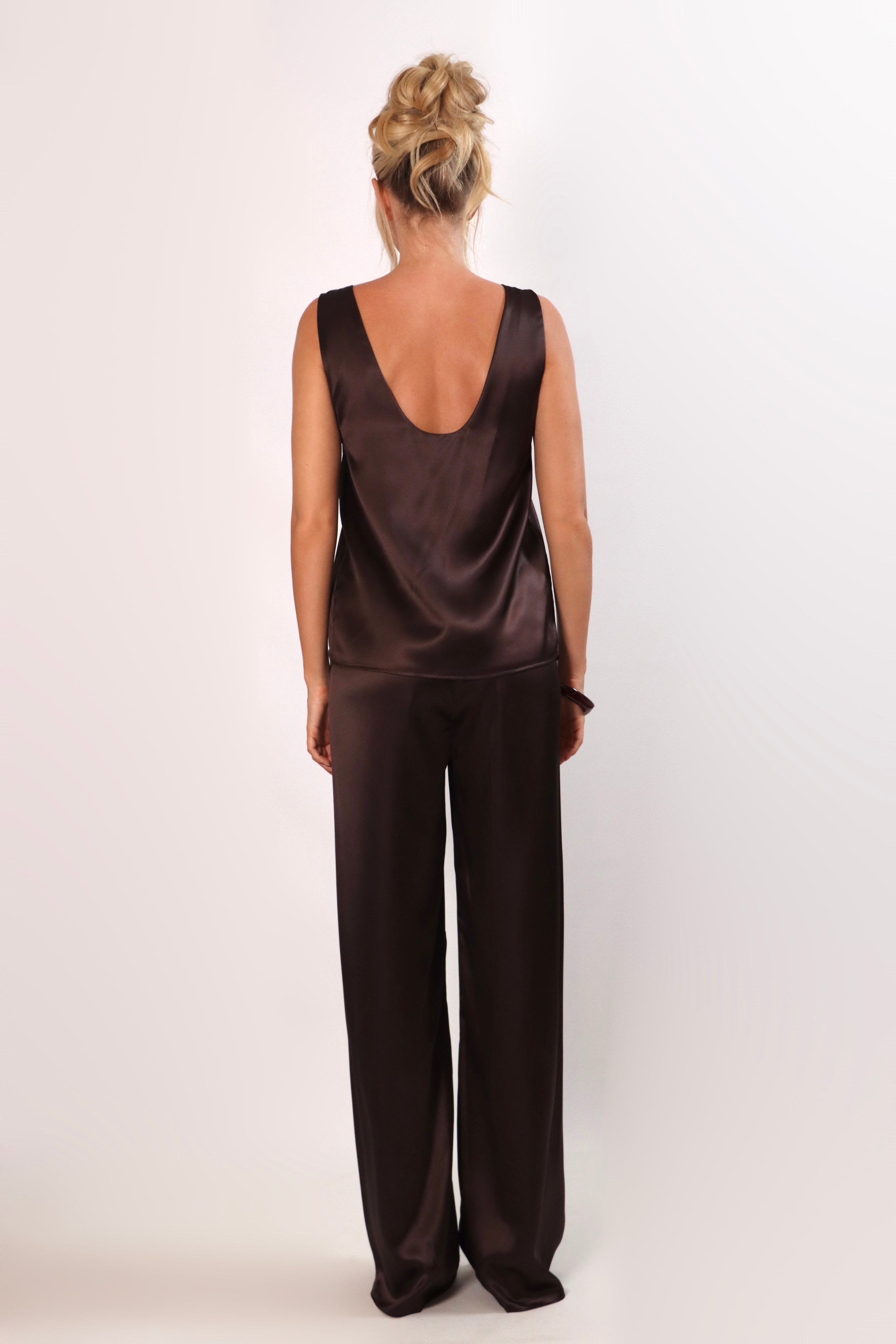 Model wearing a brown satin sleeveless top with a deep plunging neckline and matching satin pants for a sleek monochrome look.