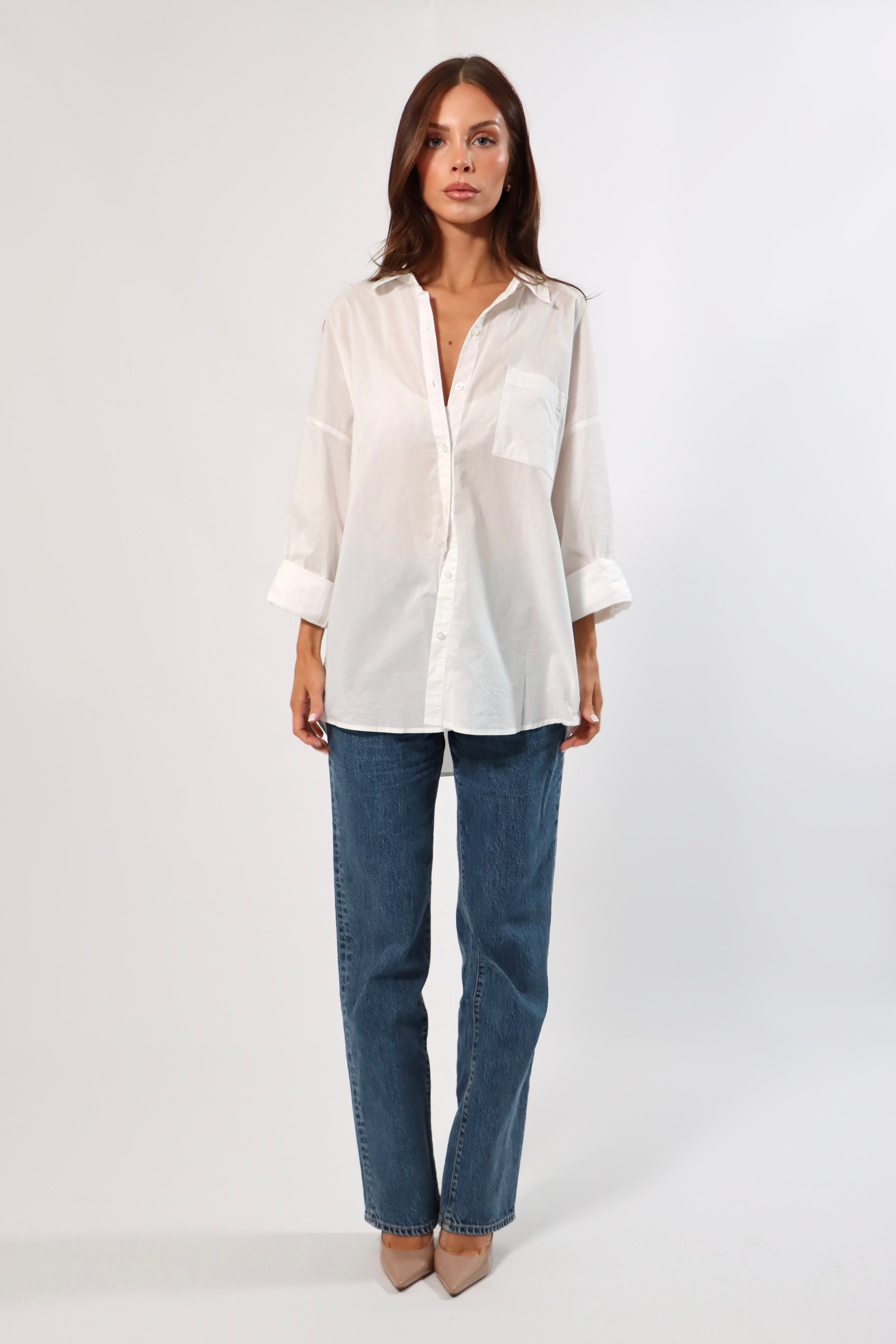 Woman in a white cotton oversized shirt with front pocket and blue jeans.