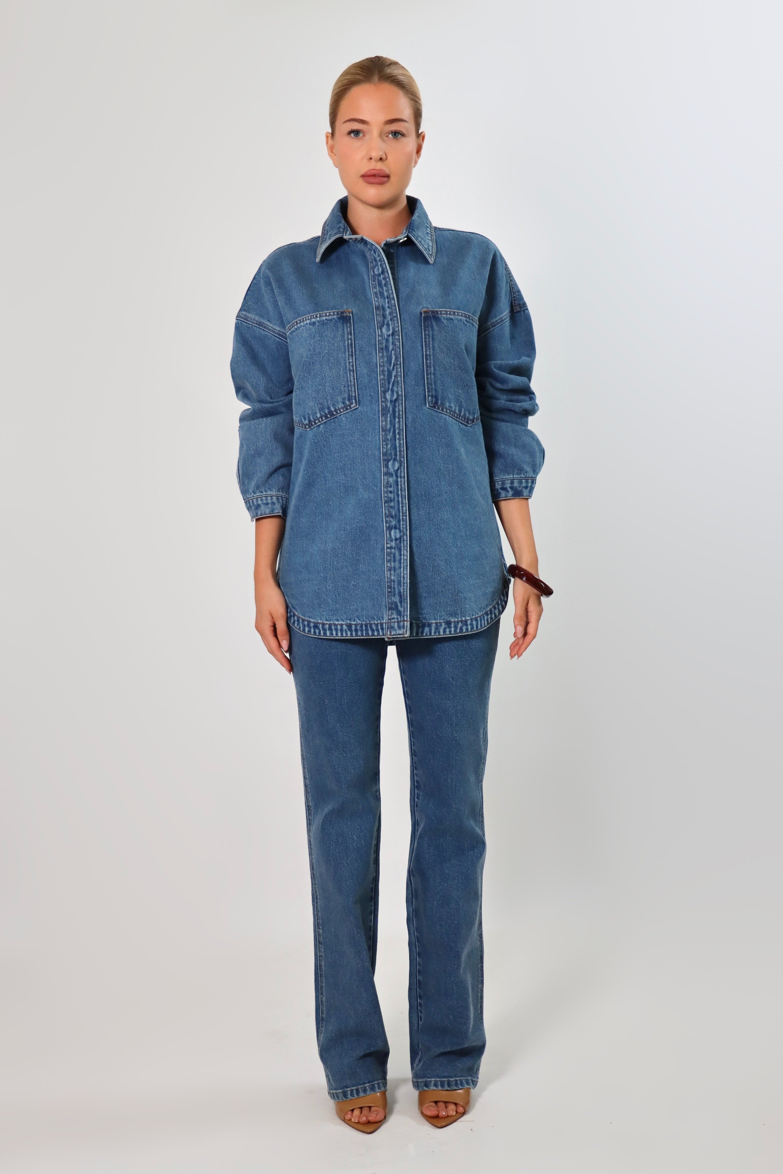 Woman wearing an oversized blue denim shirt jacket made from heavy structured denim, featuring large front pockets and long sleeves, styled with matching Stella Jeans for a full denim-on-denim look.