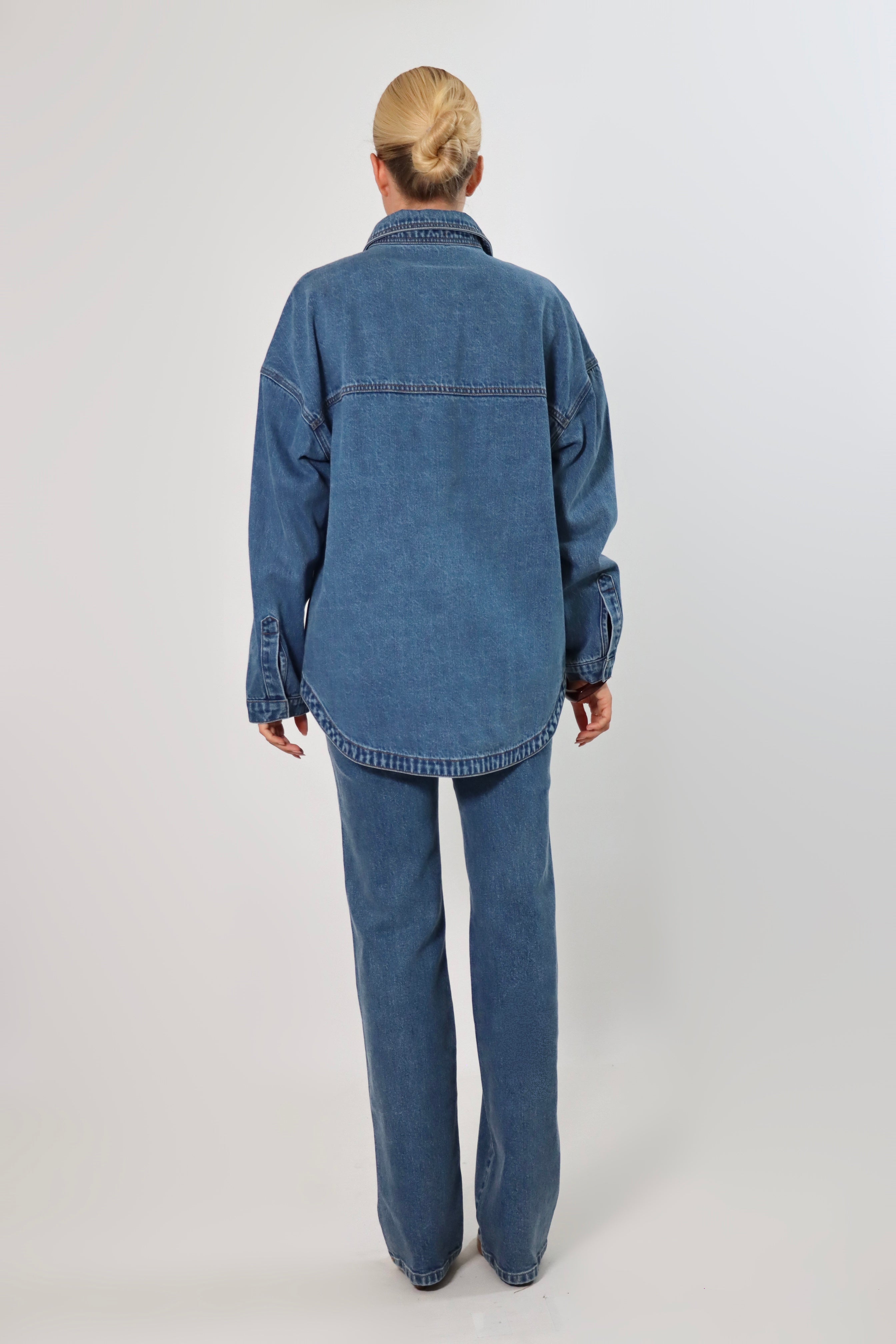 Woman wearing an oversized blue denim shirt jacket made from heavy structured denim, featuring large front pockets and long sleeves, styled with matching Stella Jeans for a full denim-on-denim look.