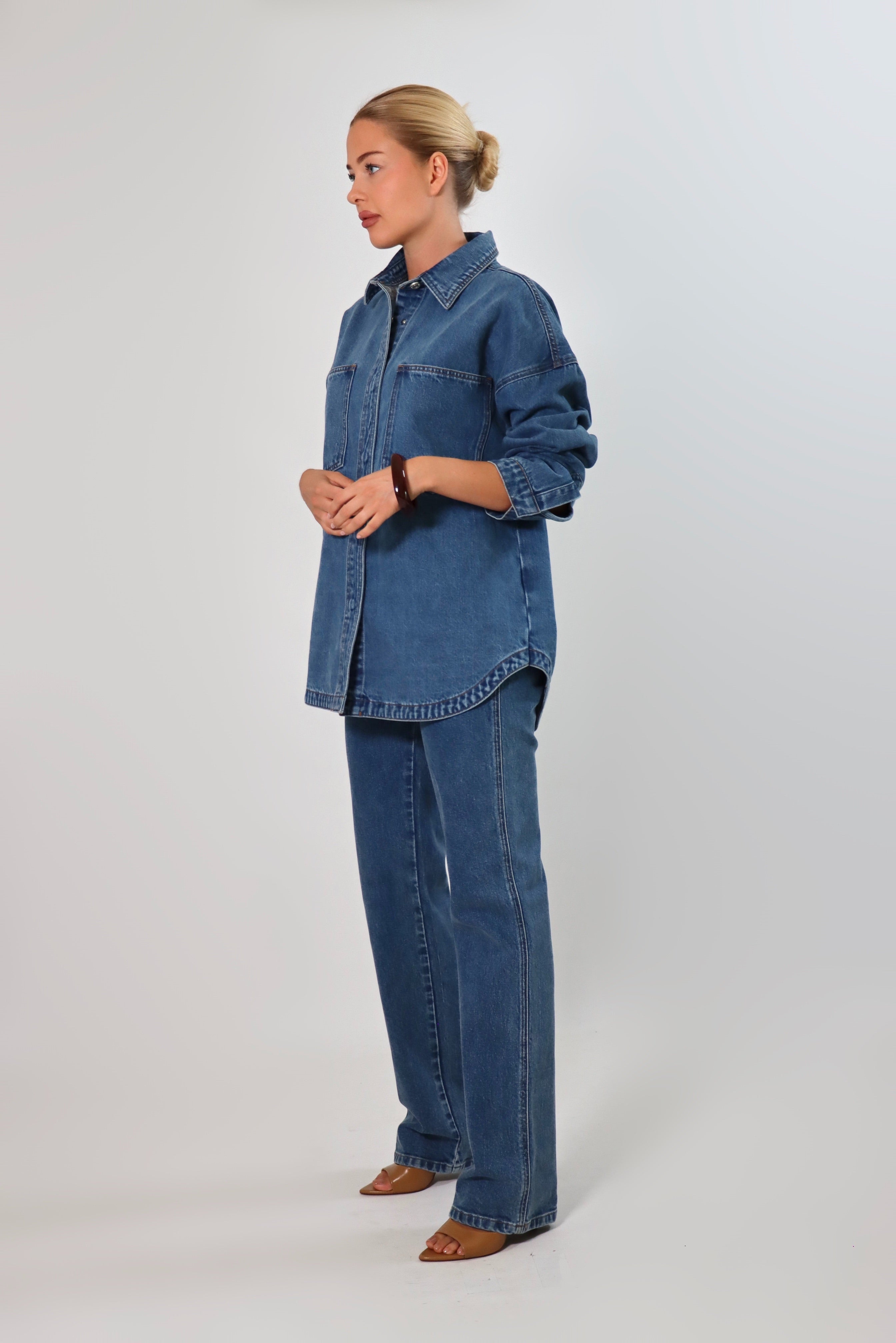 Woman wearing an oversized blue denim shirt jacket made from heavy structured denim, featuring large front pockets and long sleeves, styled with matching Stella Jeans for a full denim-on-denim look.