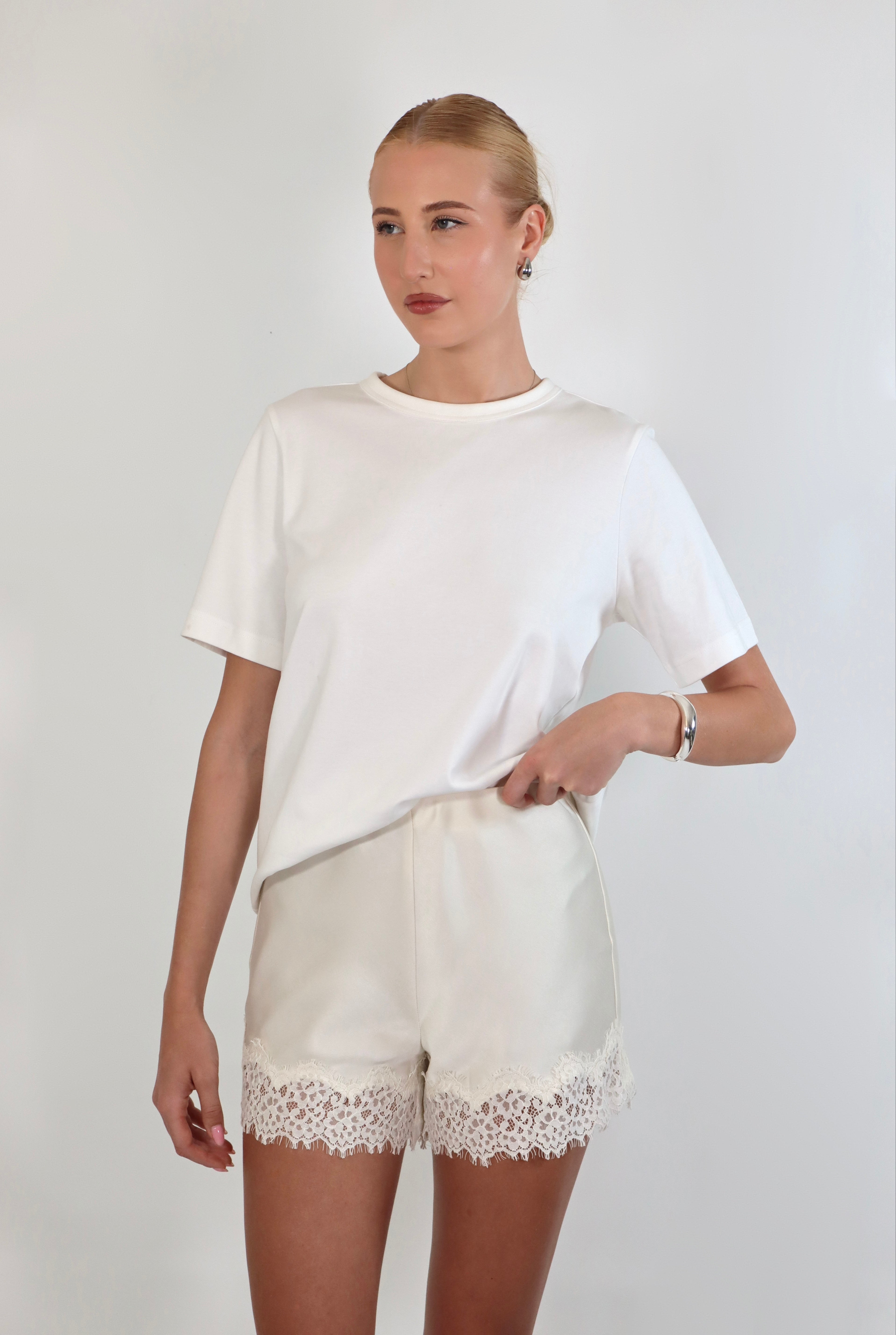 Woman wearing a relaxed white crewneck tee paired with ivory satin shorts featuring delicate lace trim.