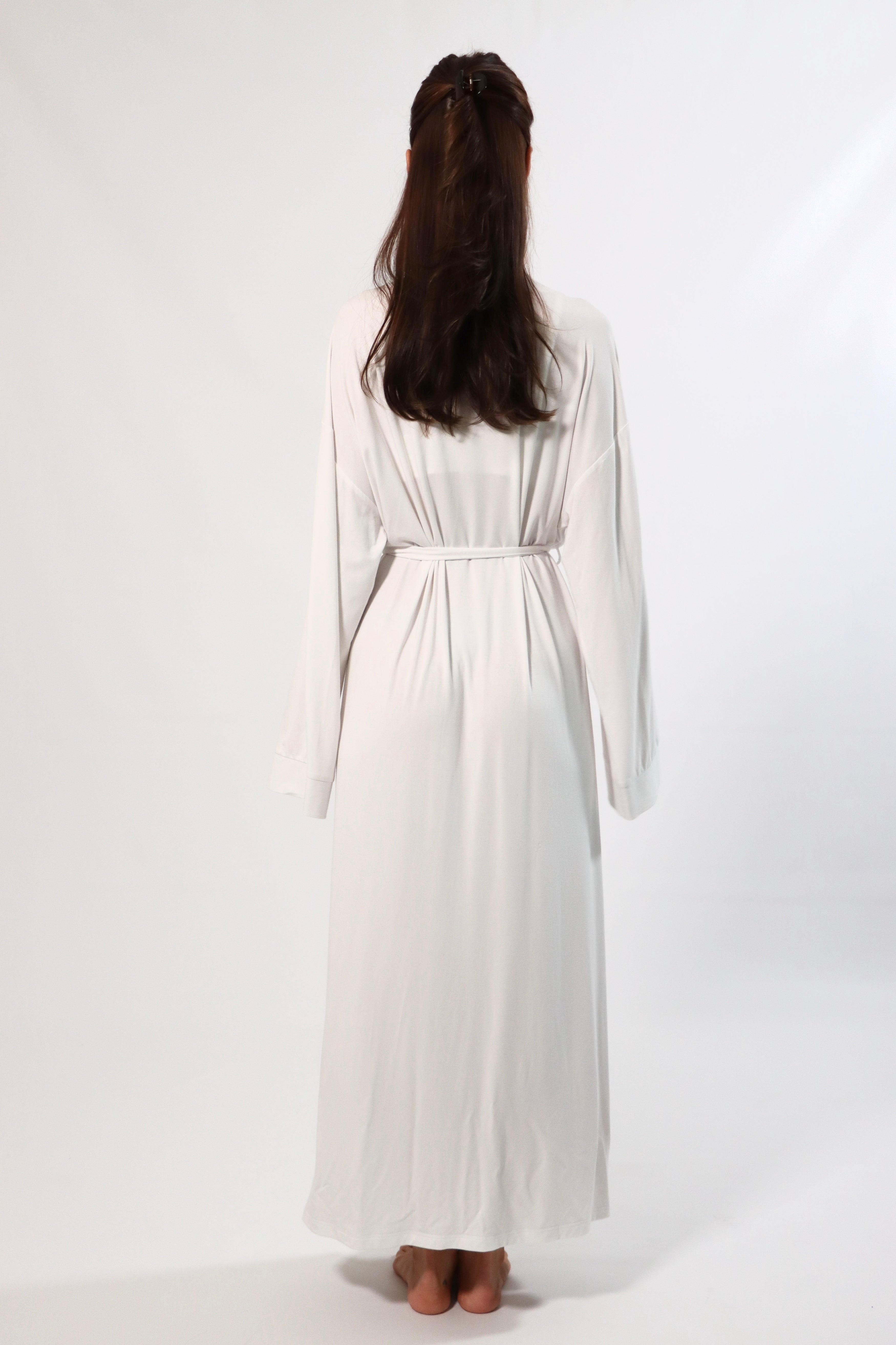 Back view of a woman in a long white robe with bell sleeves and tie waist.