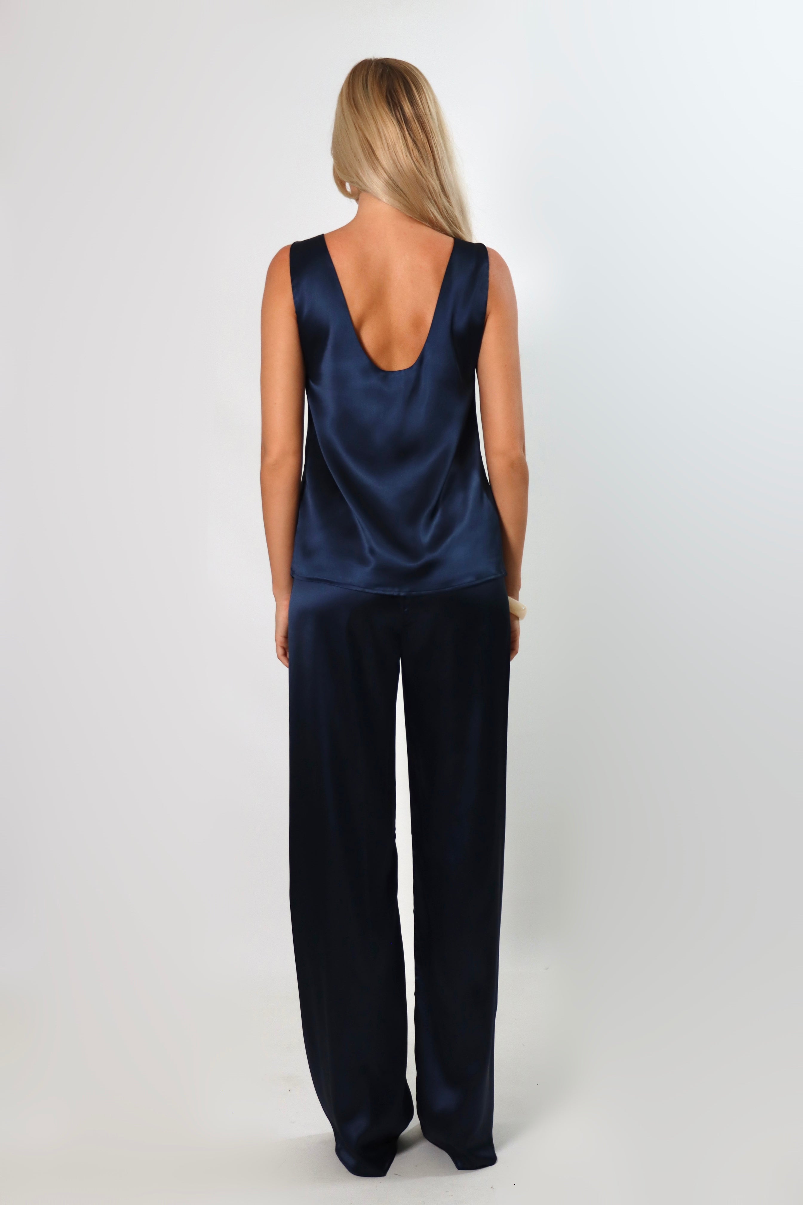 Model wearing a navy satin sleeveless top with a deep plunging neckline and relaxed fit, styled with matching satin pants against a neutral background.