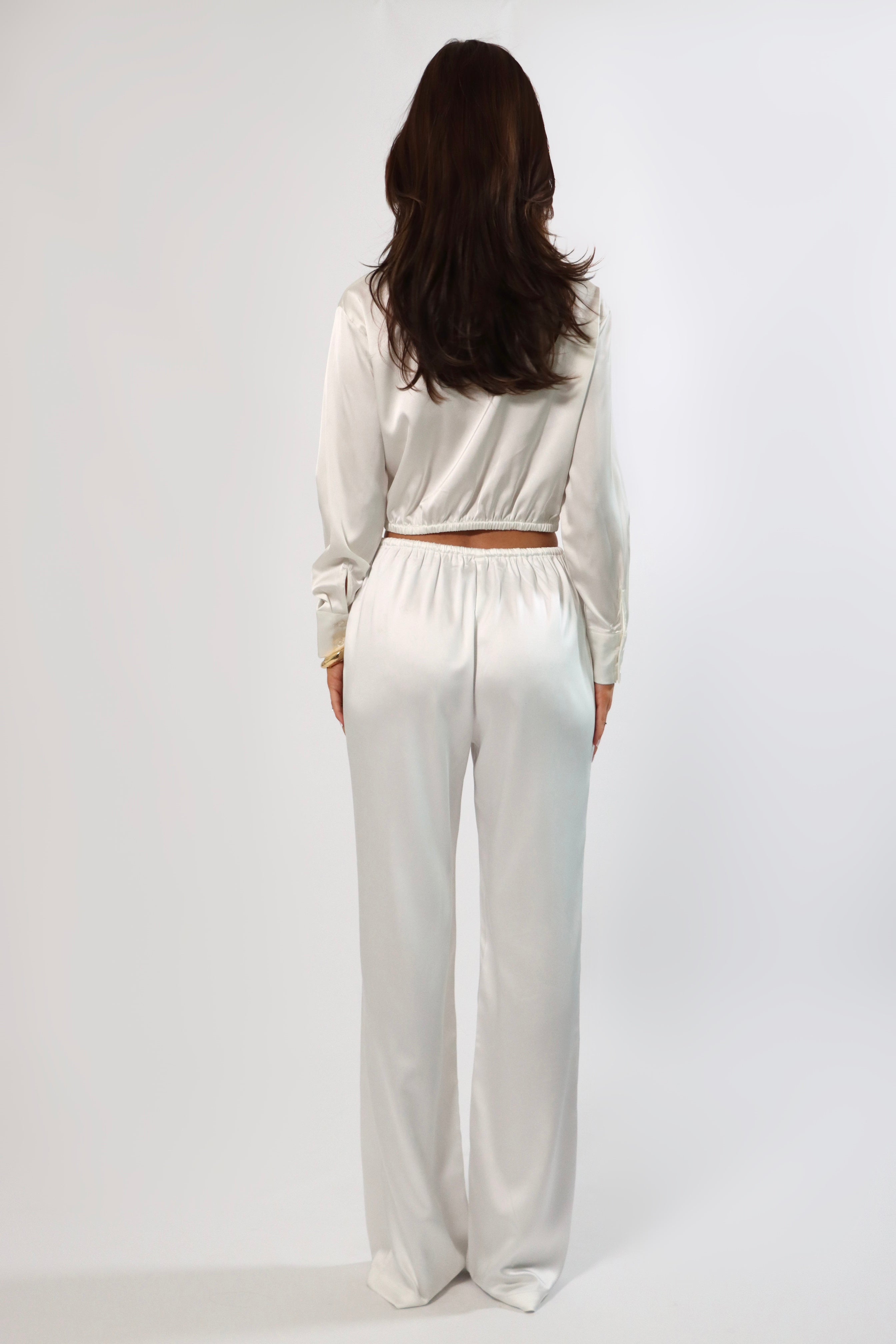 Back view of woman in white satin drawstring pants and matching long sleeve top.