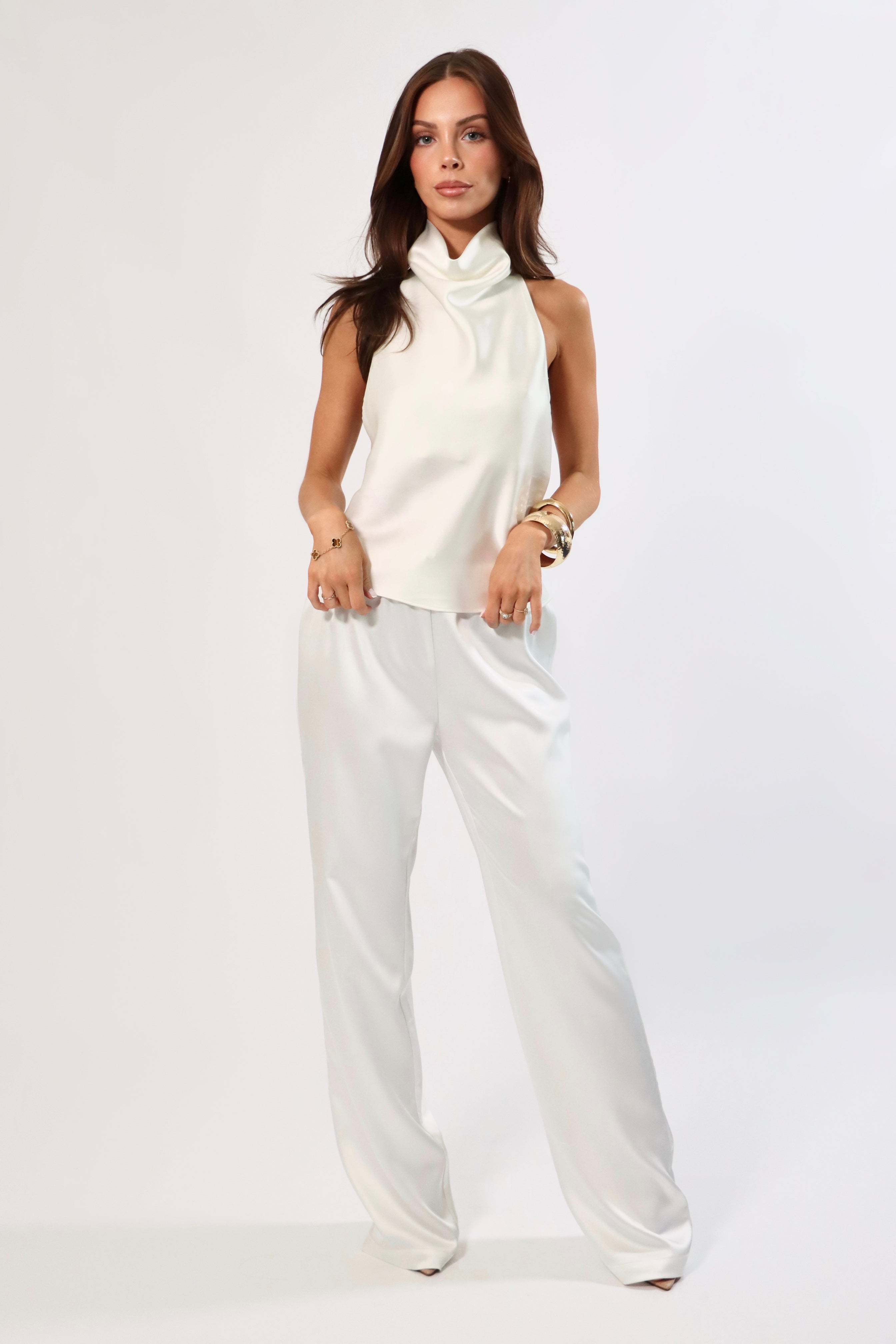 Woman in white satin cowl neck top and wide-leg pants. Backless design detail visible.