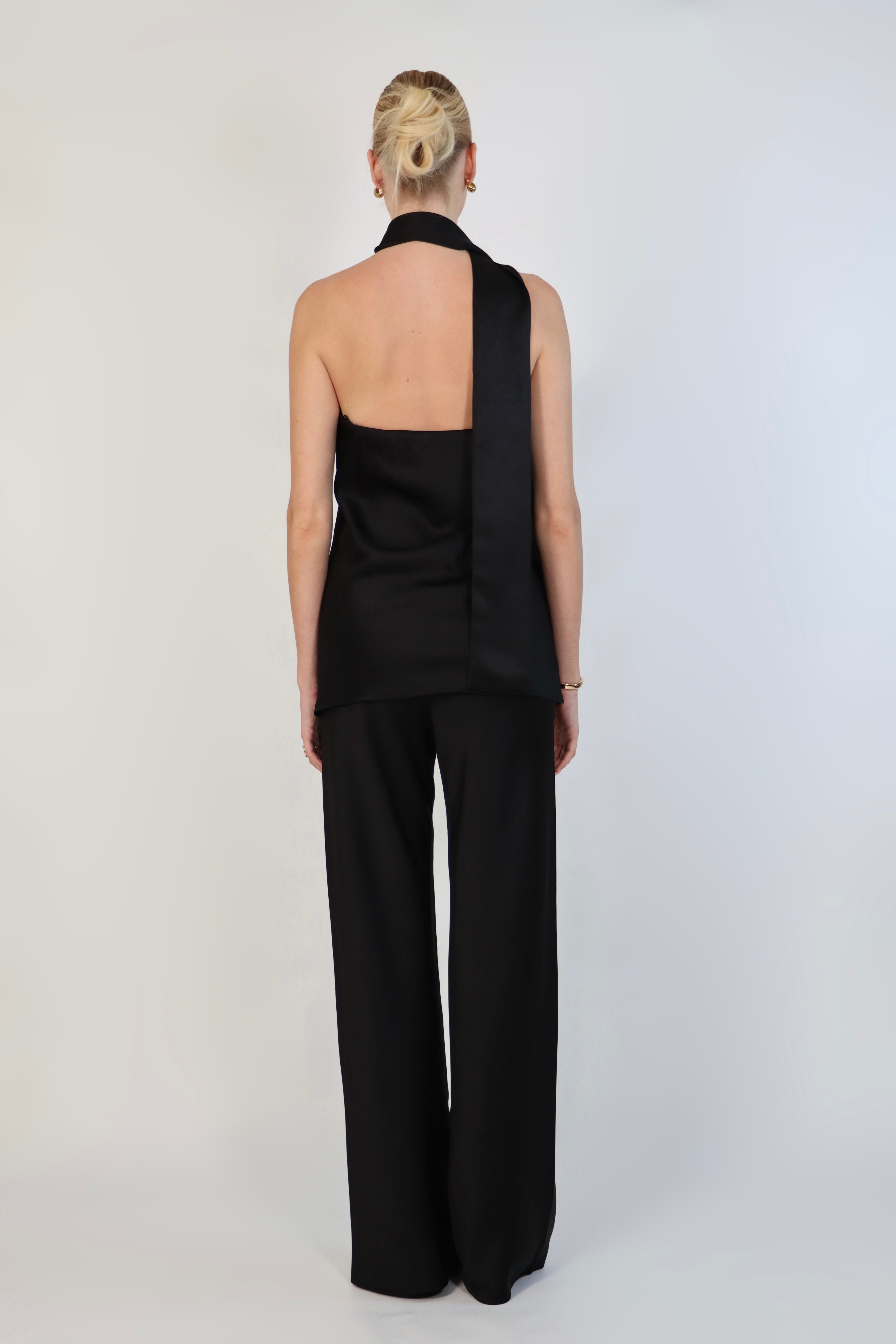 A model wearing a black, strapless satin top with a matching scarf wrapped elegantly around her neck. The top has a clean, structured bodice and is paired with matching April Satin Pants for a monochromatic, sophisticated look against a plain white background.