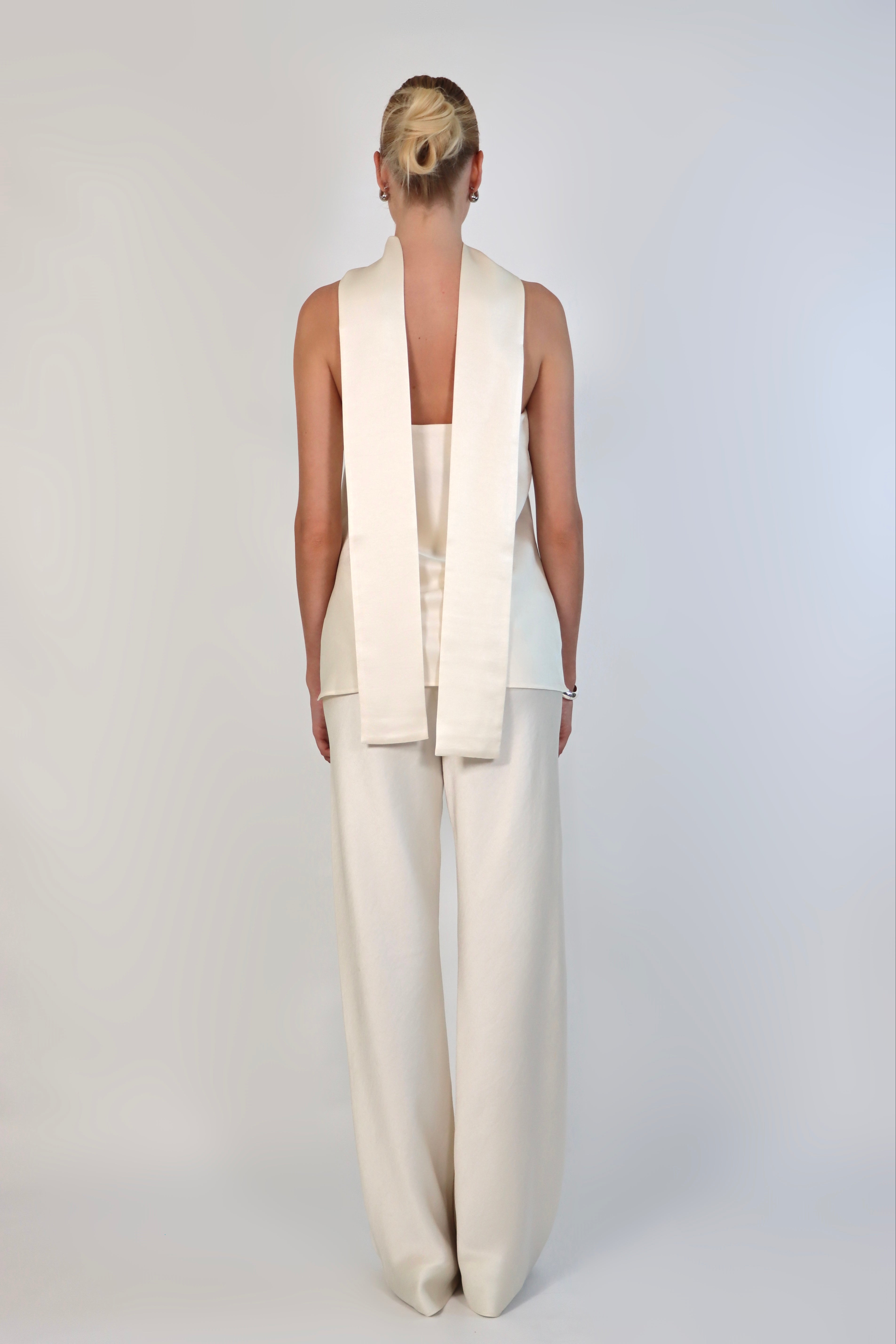 A model wearing a cream-colored, strapless satin top with a matching scarf wrapped elegantly around her neck. The top has a clean, structured bodice and is paired with matching April Satin Pants for a monochromatic, sophisticated look against a plain white background.