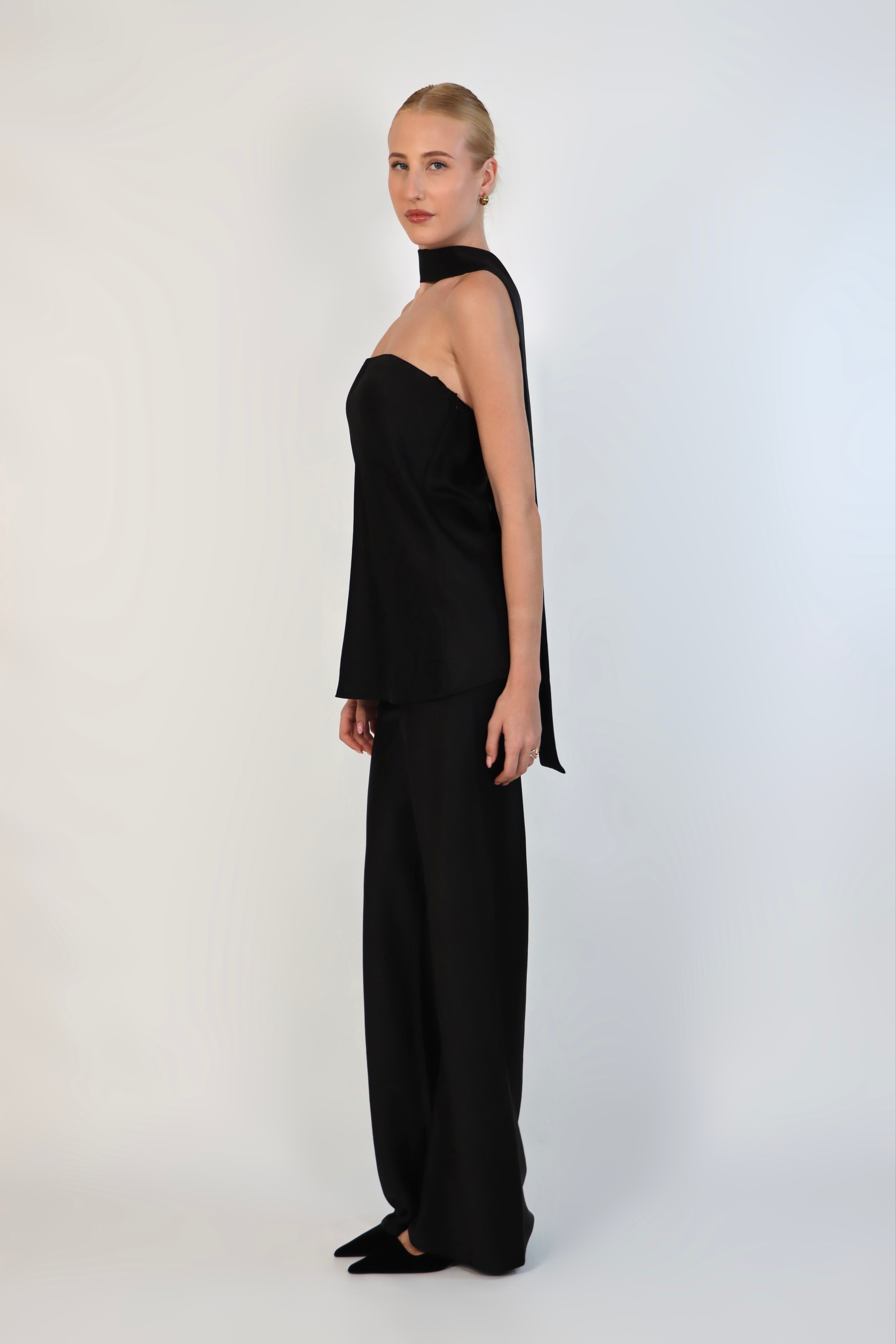A model wearing a black, strapless satin top with a matching scarf wrapped elegantly around her neck. The top has a clean, structured bodice and is paired with matching April Satin Pants for a monochromatic, sophisticated look against a plain white background.