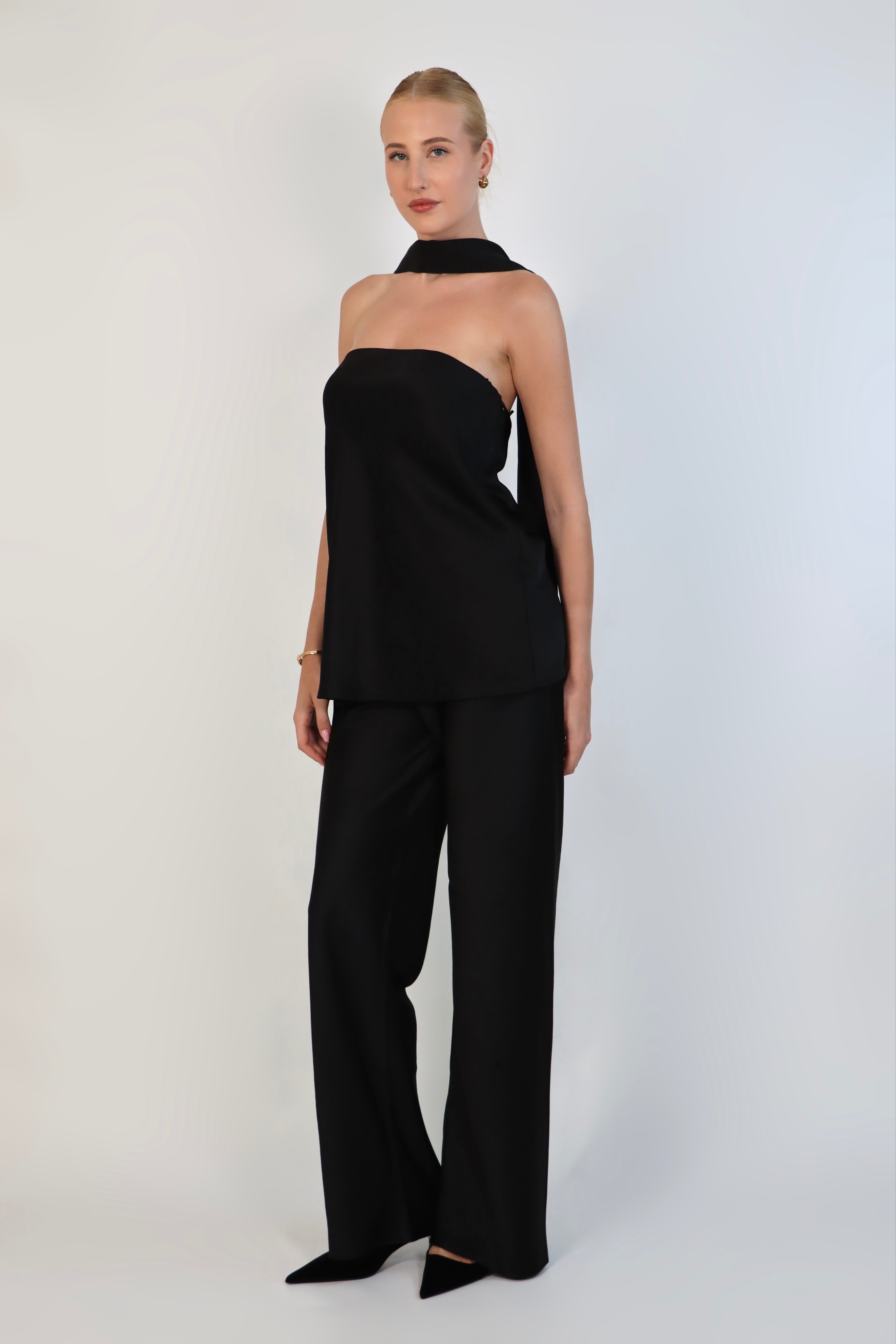 A model wearing a black, strapless satin top with a matching scarf wrapped elegantly around her neck. The top has a clean, structured bodice and is paired with matching April Satin Pants for a monochromatic, sophisticated look against a plain white background.