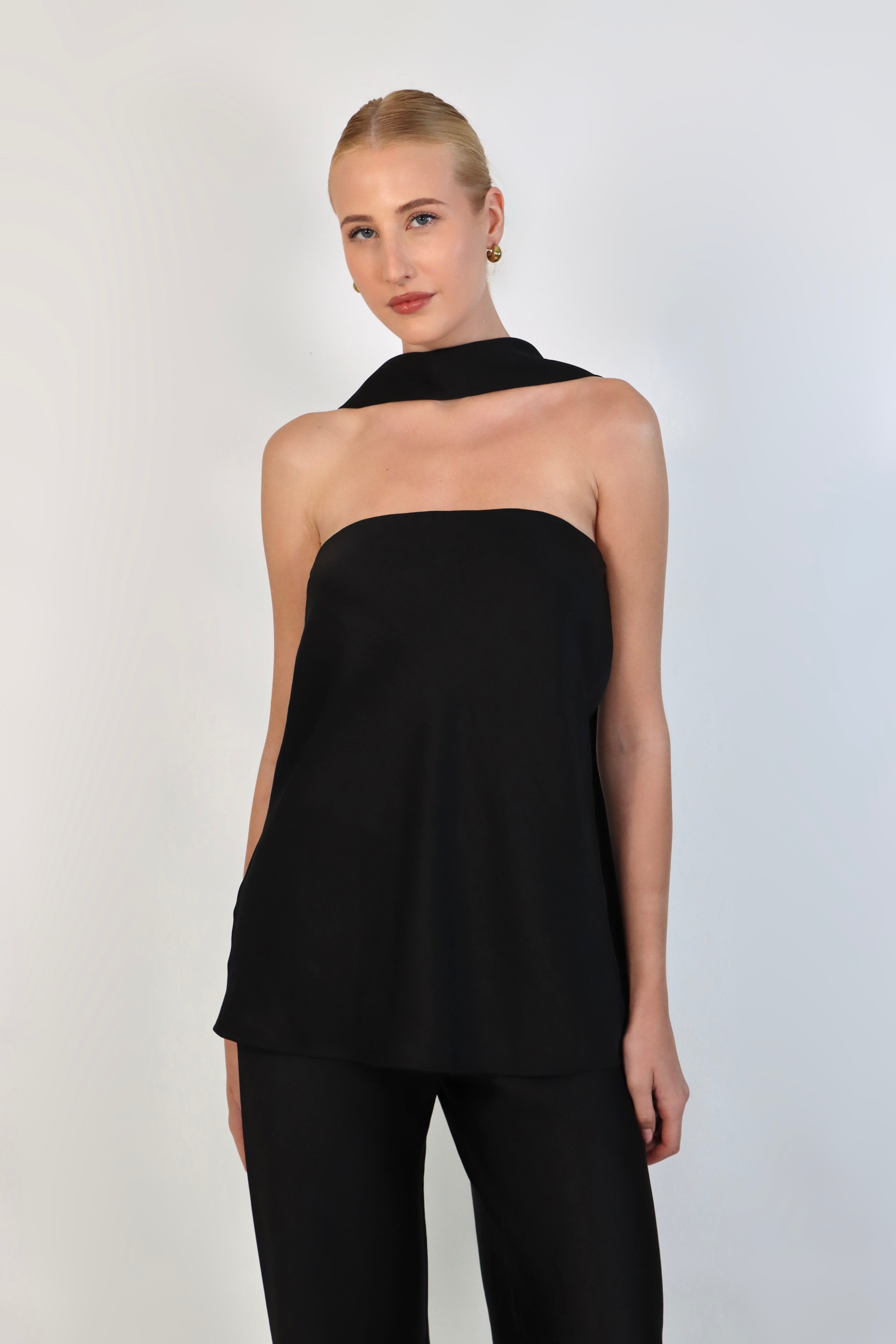 A model wearing a black, strapless satin top with a matching scarf wrapped elegantly around her neck. The top has a clean, structured bodice and is paired with matching April Satin Pants for a monochromatic, sophisticated look against a plain white background.