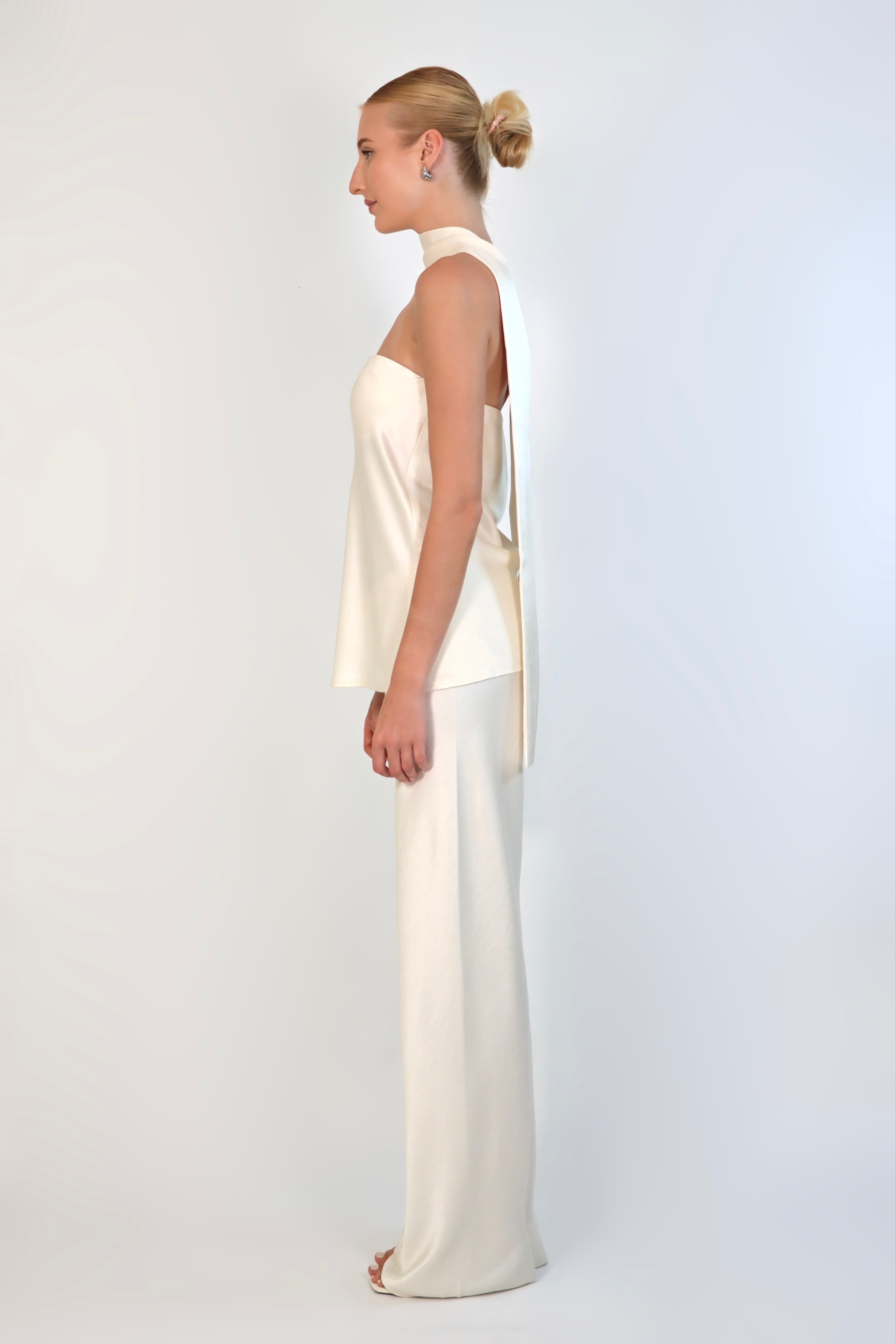 A model wearing a cream-colored, strapless satin top with a matching scarf wrapped elegantly around her neck. The top has a clean, structured bodice and is paired with matching April Satin Pants for a monochromatic, sophisticated look against a plain white background.