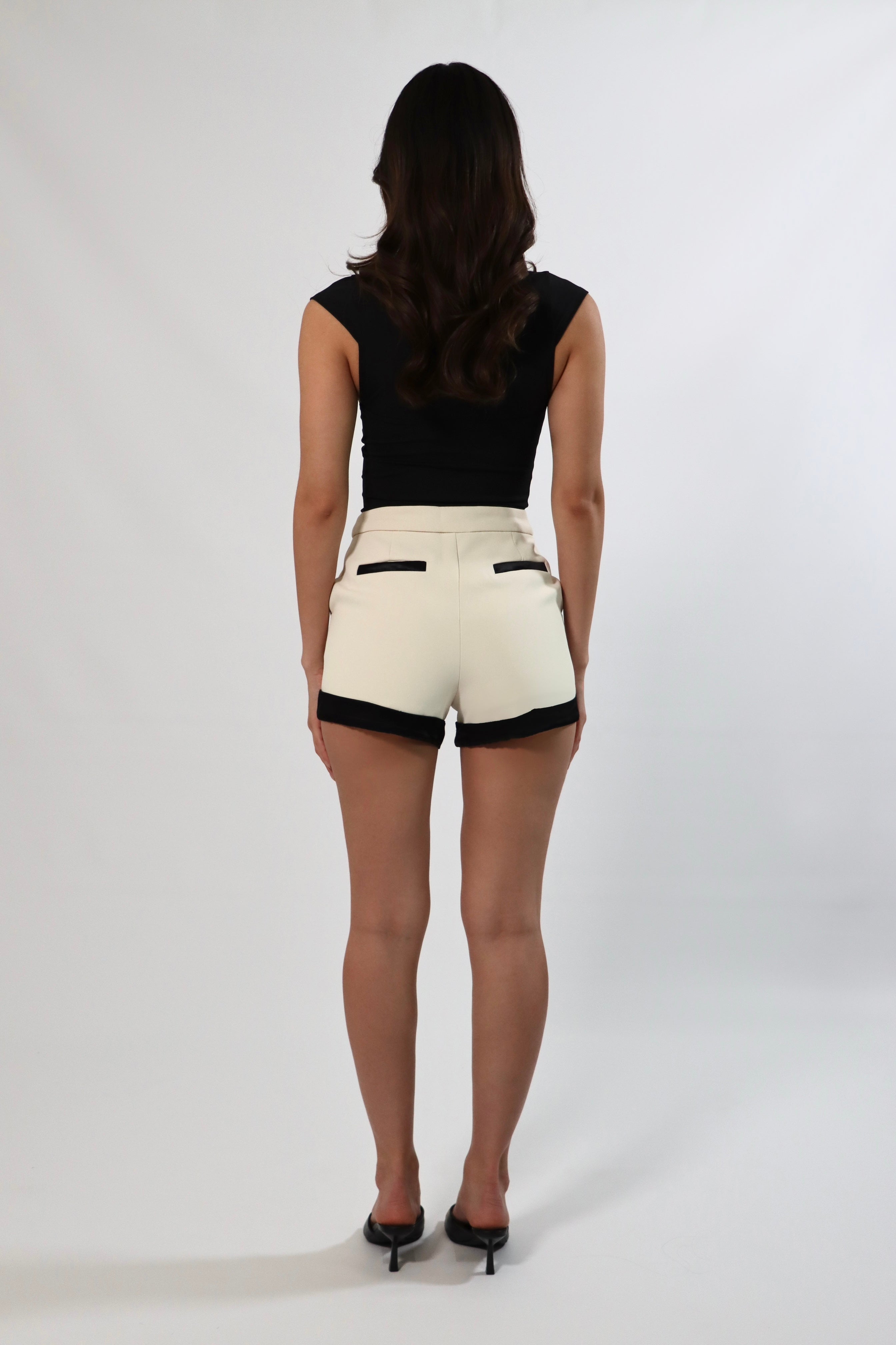 Back view of woman in high-waisted shorts with satin trim and pockets, paired with black top and heels.