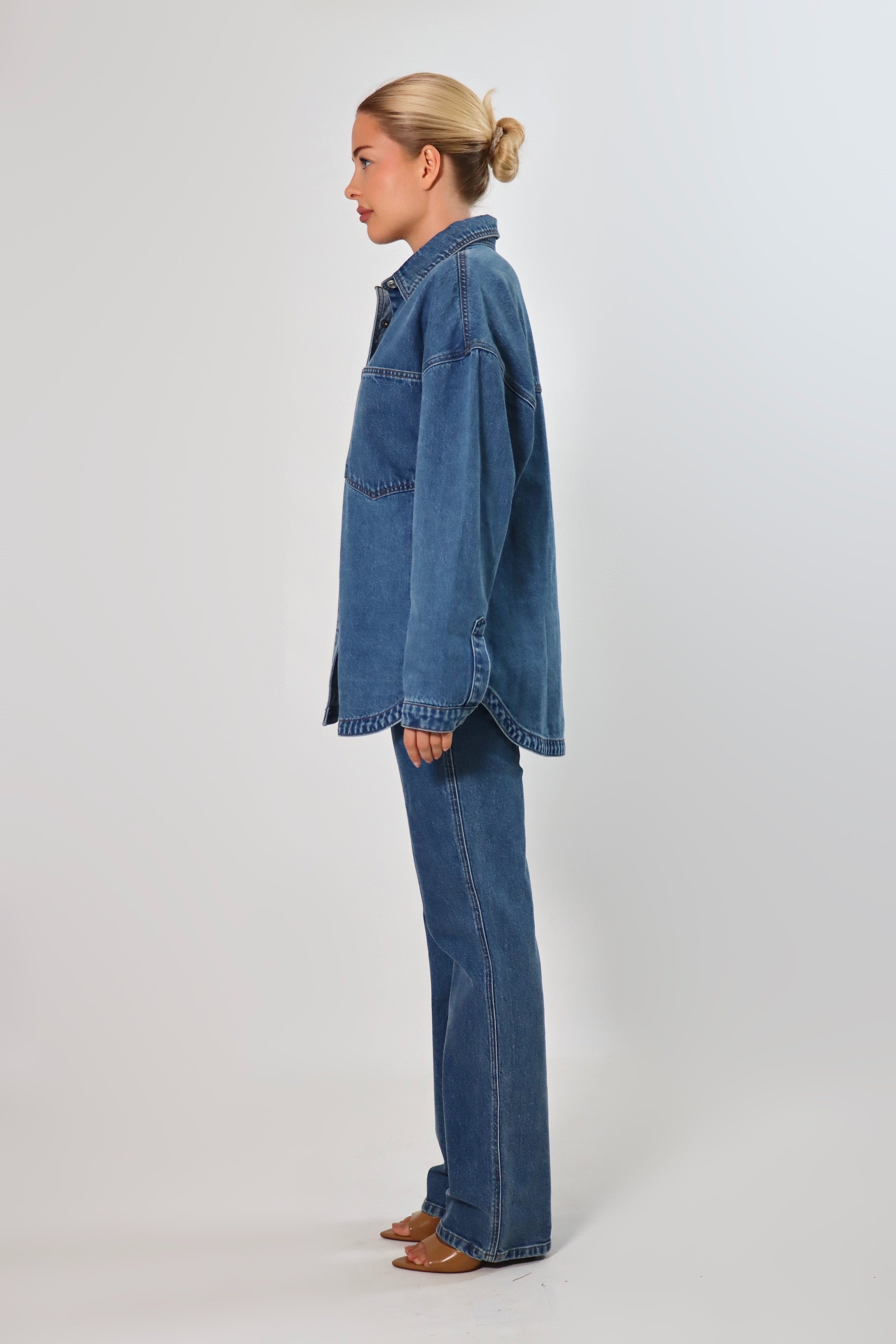 Woman wearing an oversized blue denim shirt jacket made from heavy structured denim, featuring large front pockets and long sleeves, styled with matching Stella Jeans for a full denim-on-denim look.