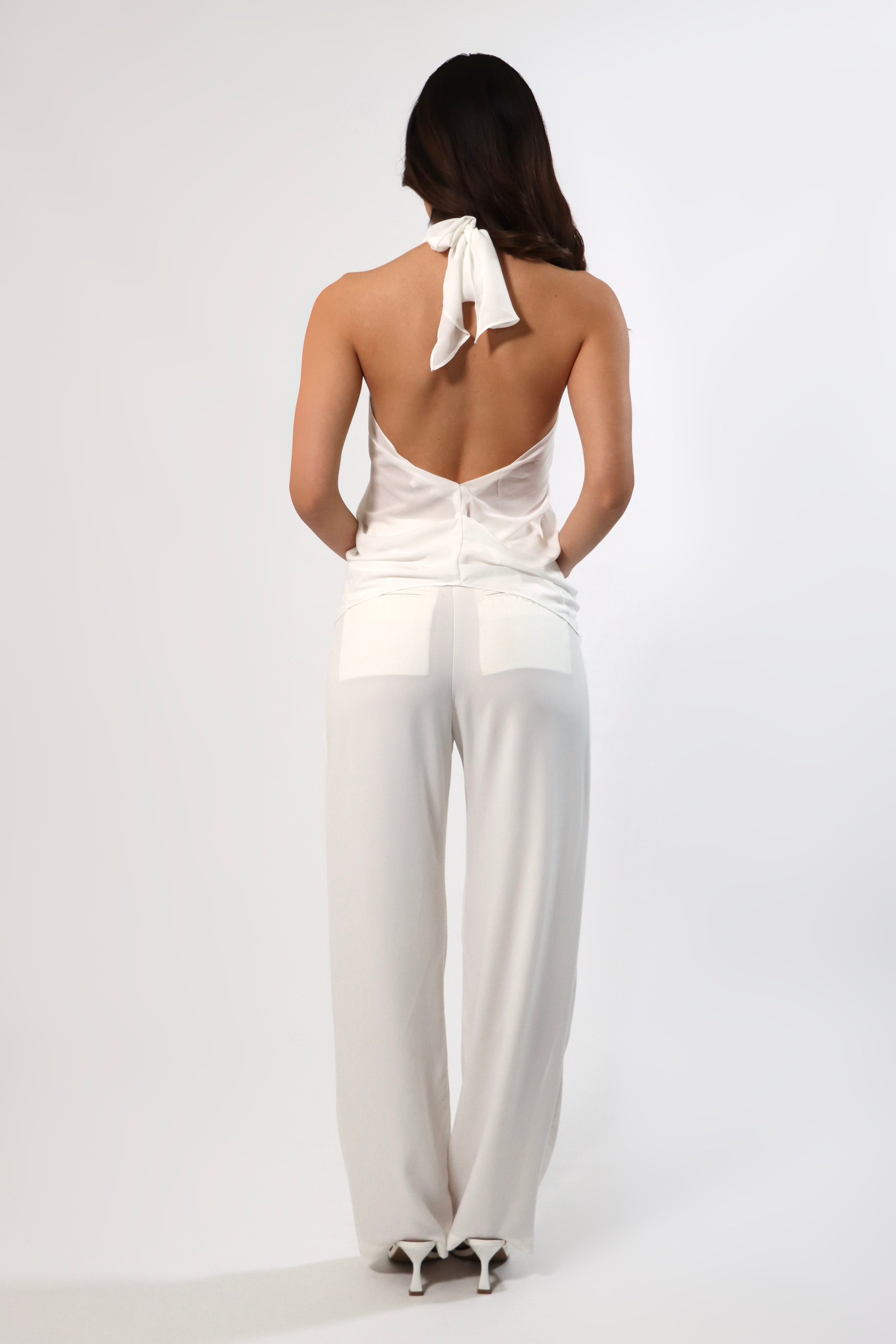 Back view of a woman wearing April Seven Olivia white halter top and straight leg pants with pockets.