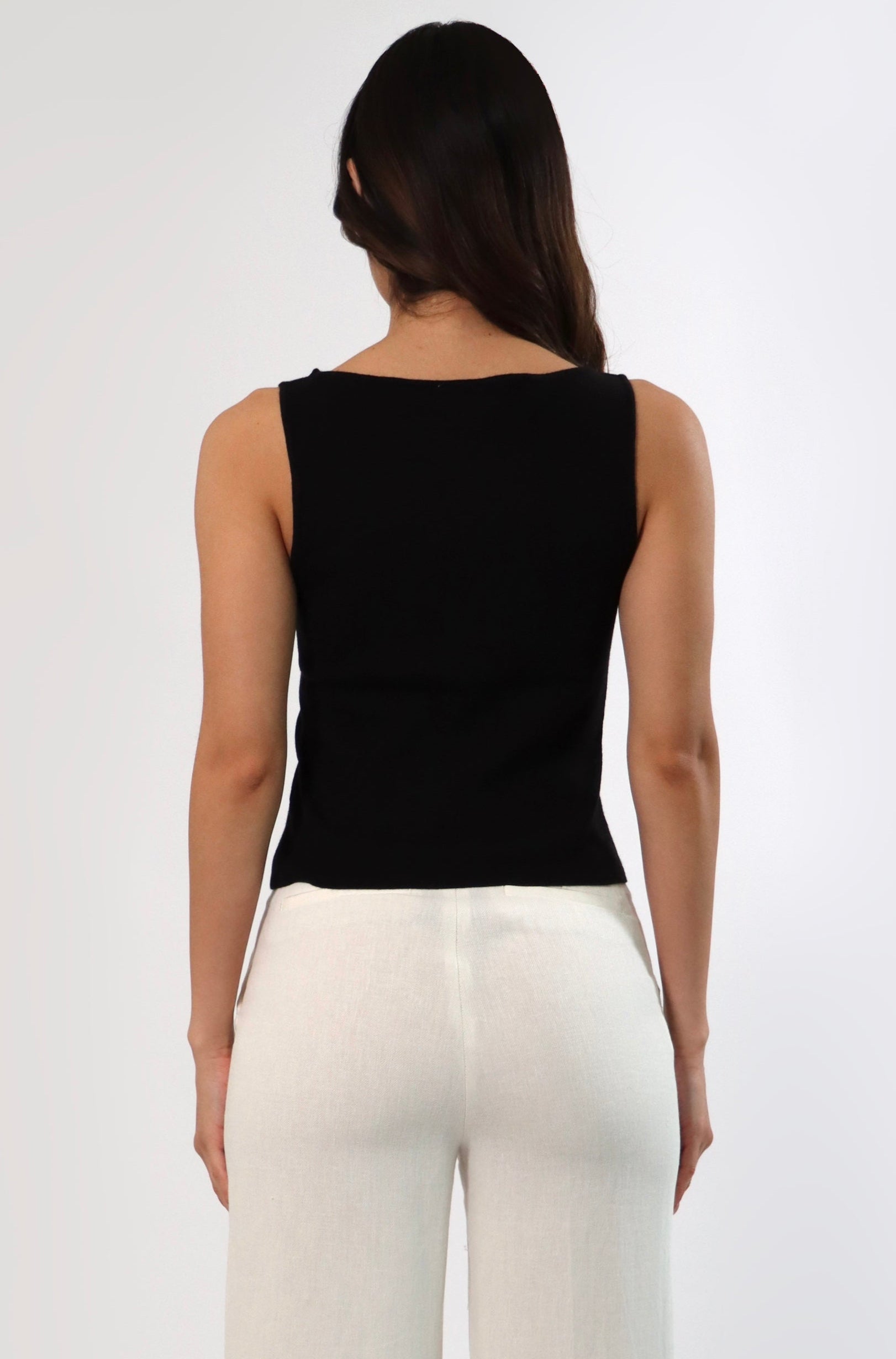 Back view of woman in black sleeveless boat neck sweater and cream-colored pants.