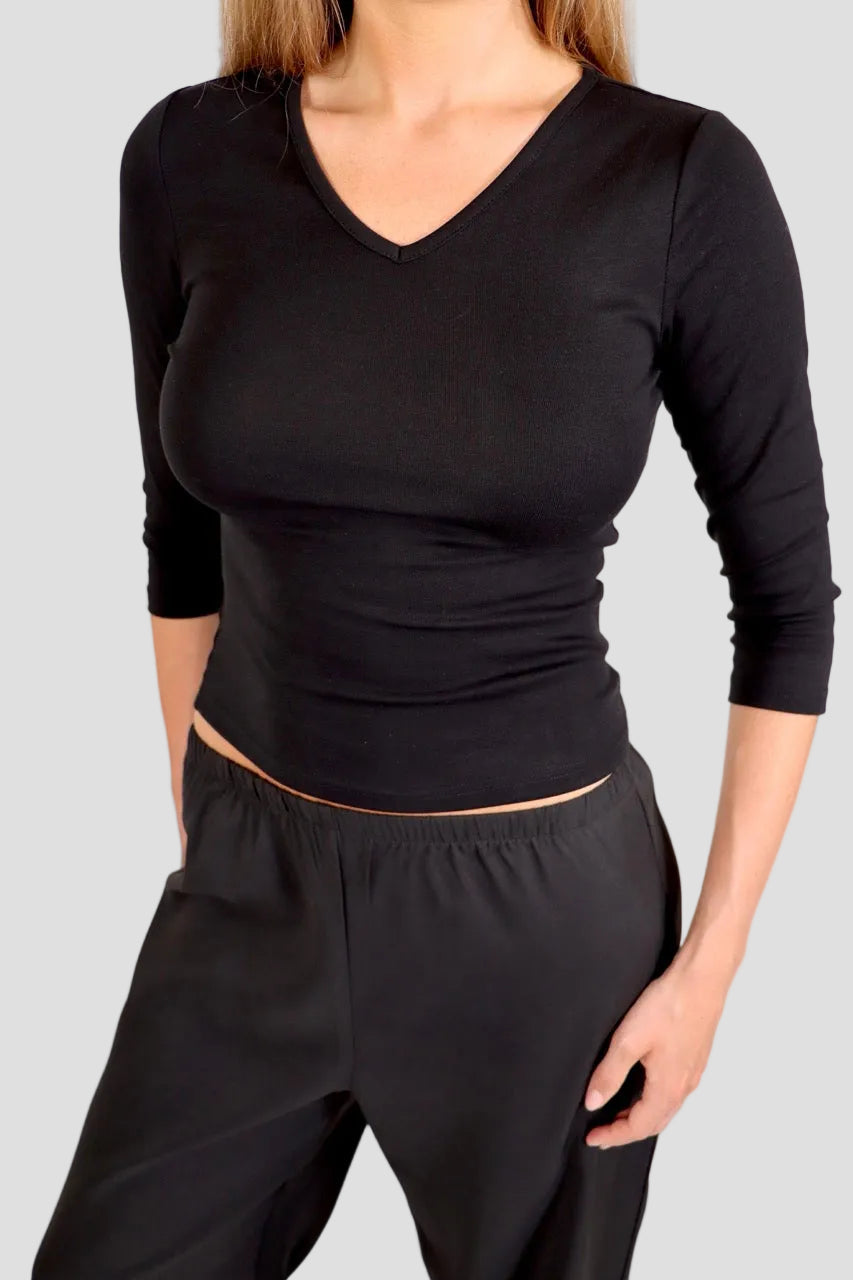 Woman wearing a black 3/4-sleeve top with V neckline and black pants against a plain background