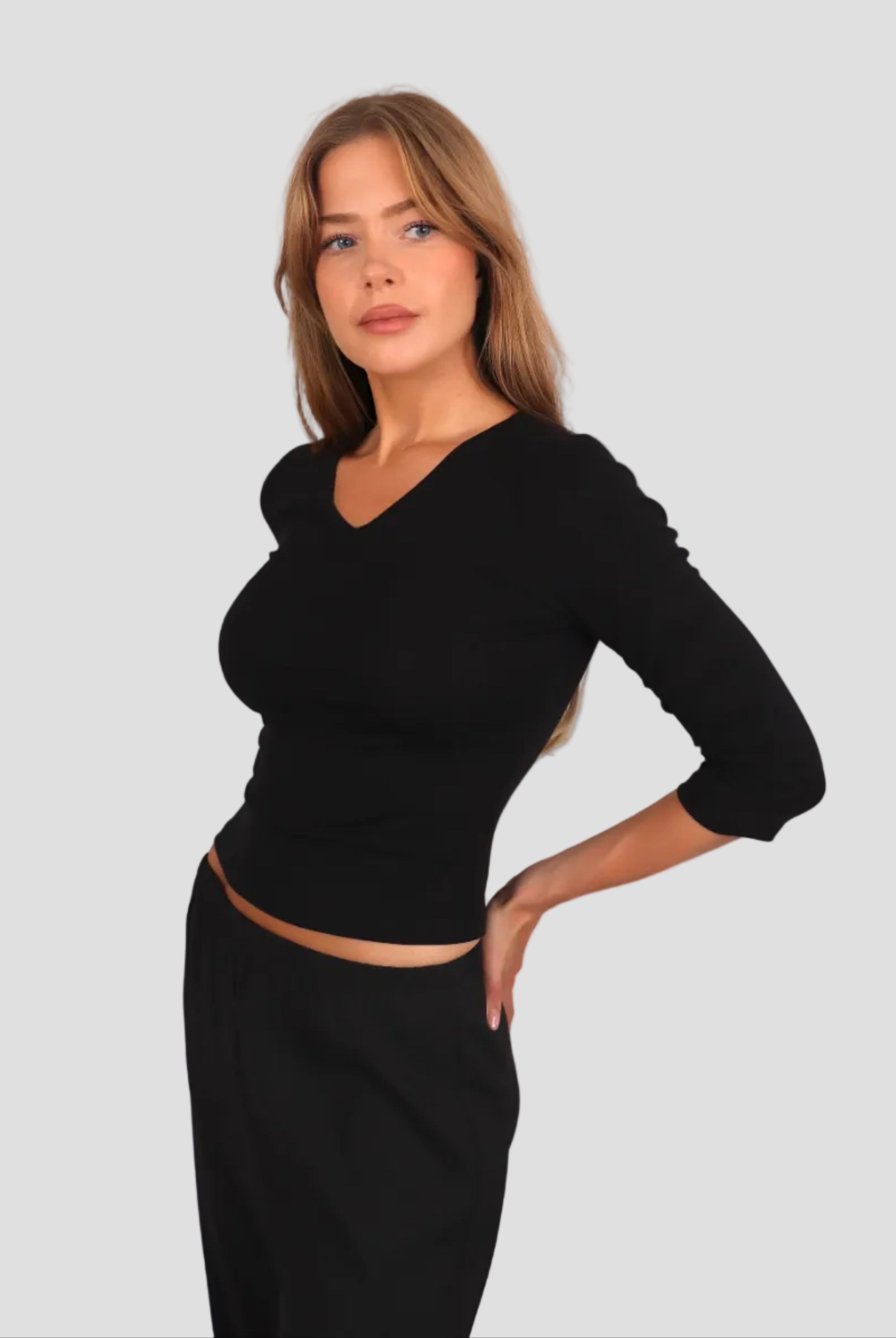Woman wearing a black 3/4-sleeve top with V neckline and black pants against a plain background