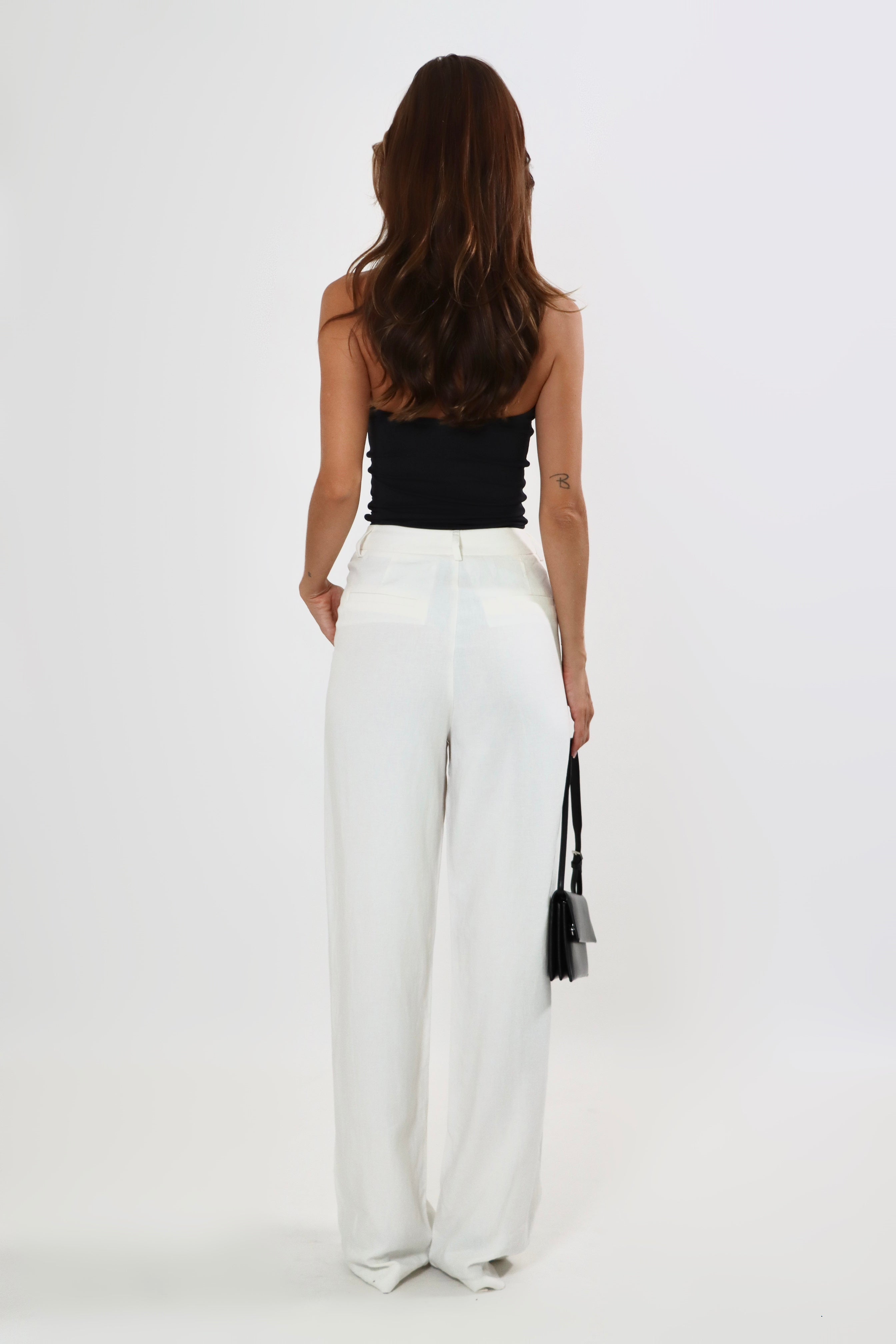Woman in high-waisted, wide-leg linen pants with button closure and black top.