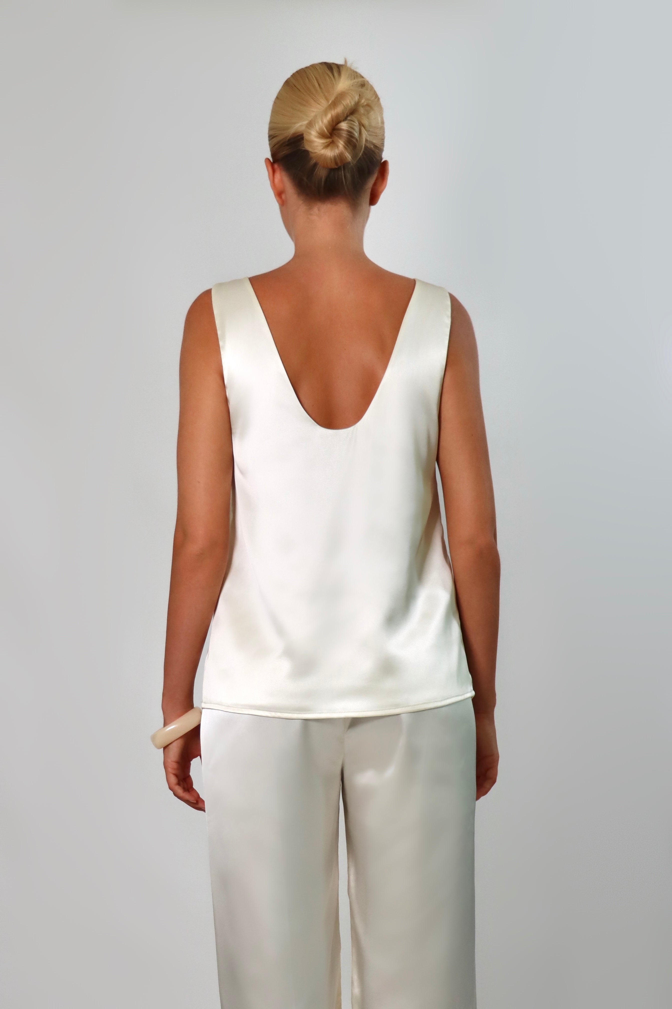 Ivory: Model wearing an ivory satin sleeveless top with a deep plunging neckline and matching satin pants against a neutral background.