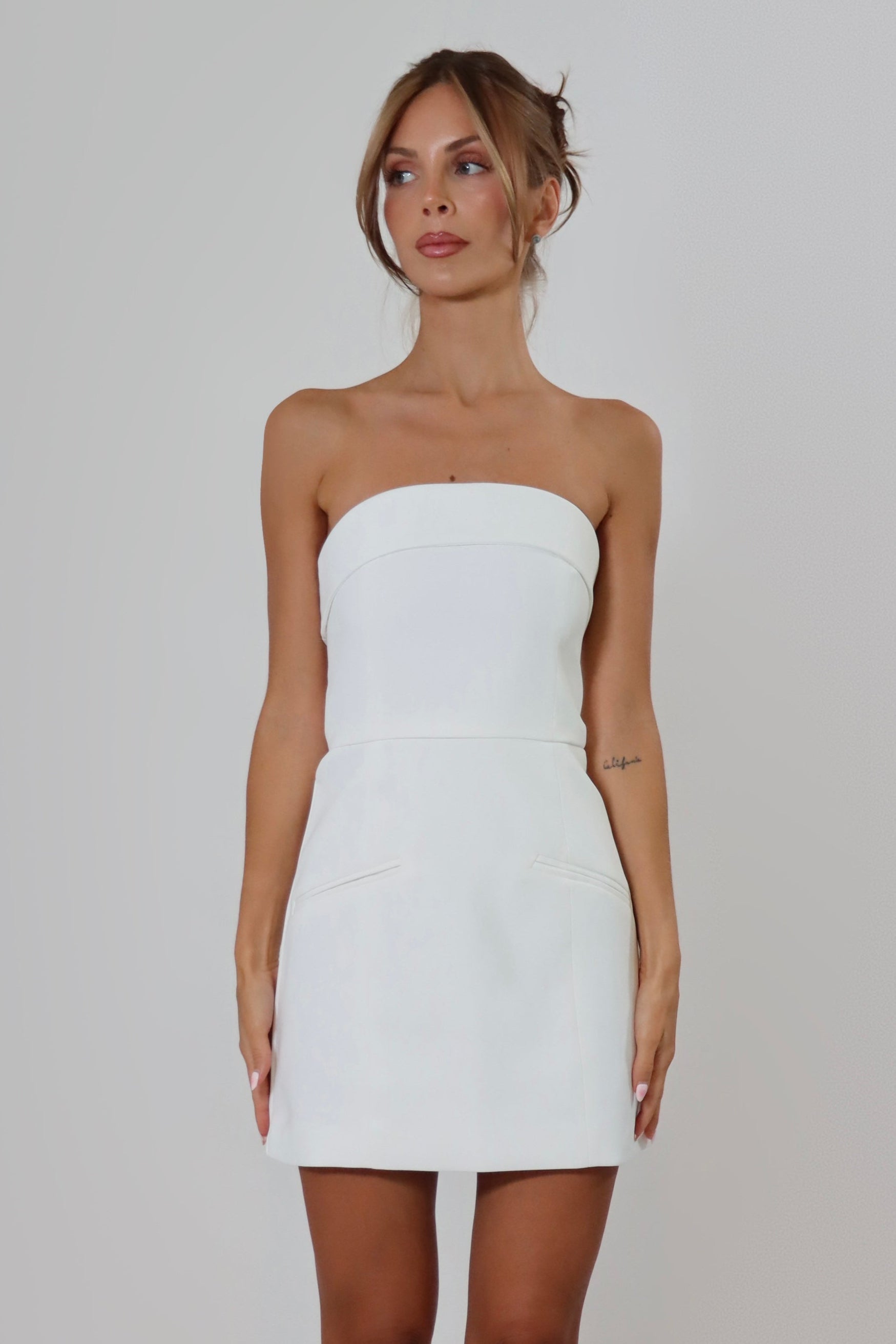 April Seven Kara Dress in white – strapless fitted mini dress with welt pocket detail, structured fabric, and full lining.