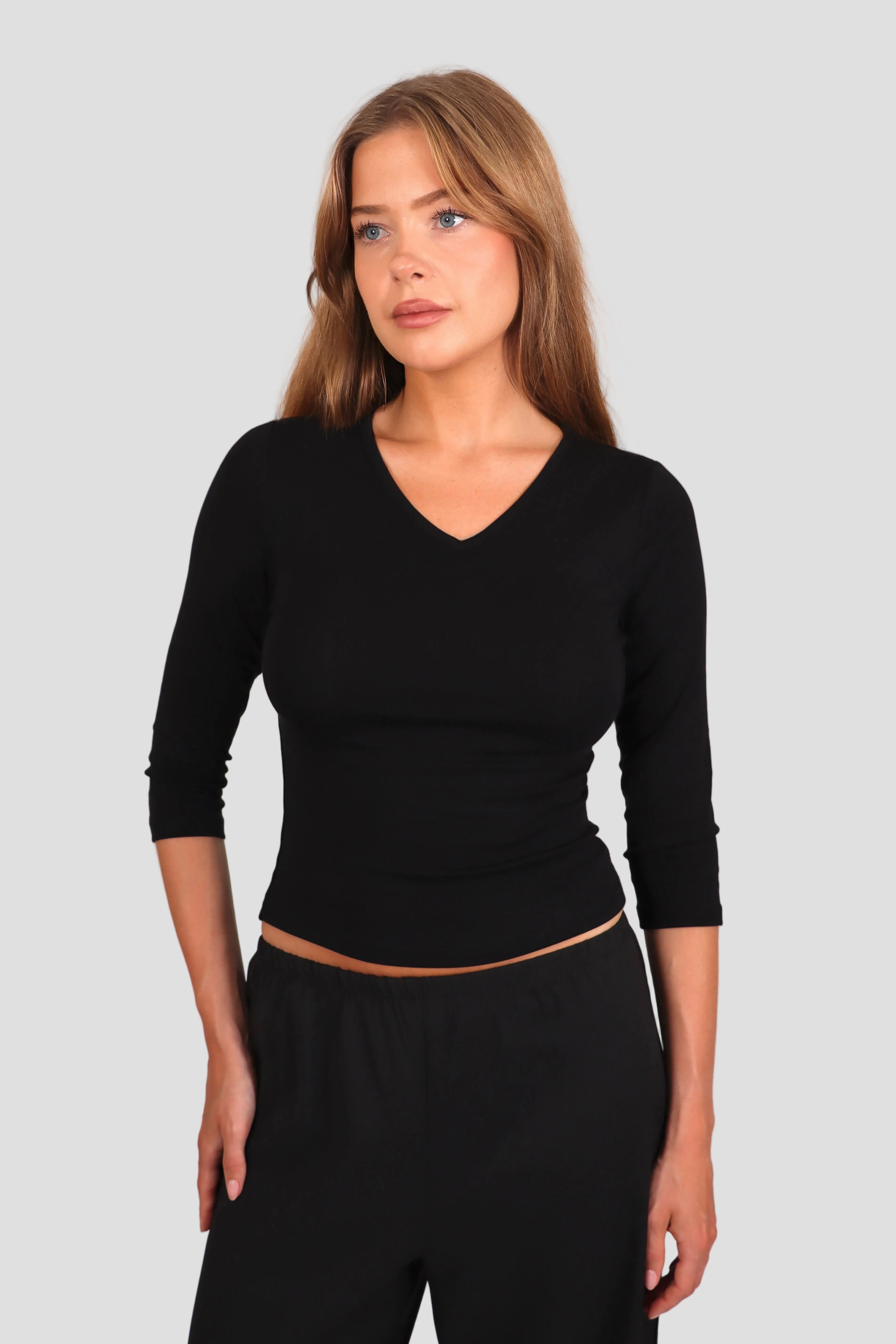 Woman wearing a black 3/4-sleeve top with V neckline and black pants against a plain background