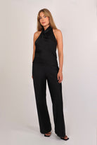 Woman wearing a black satin halter top with a draped neckline, styled with matching satin pants. The top has a smooth, glossy finish and a loose, elegant fit, creating a sophisticated and minimalist look against a light background.