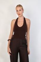 A model wearing a deep Espresso halter top with a ribbed texture and a plunging V-neckline. The fitted top is styled with matching dark brown, high-waisted tailored trousers for a sleek, monochromatic look against a white studio background.