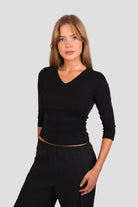 Woman wearing a black 3/4-sleeve top with V neckline and black pants against a plain background