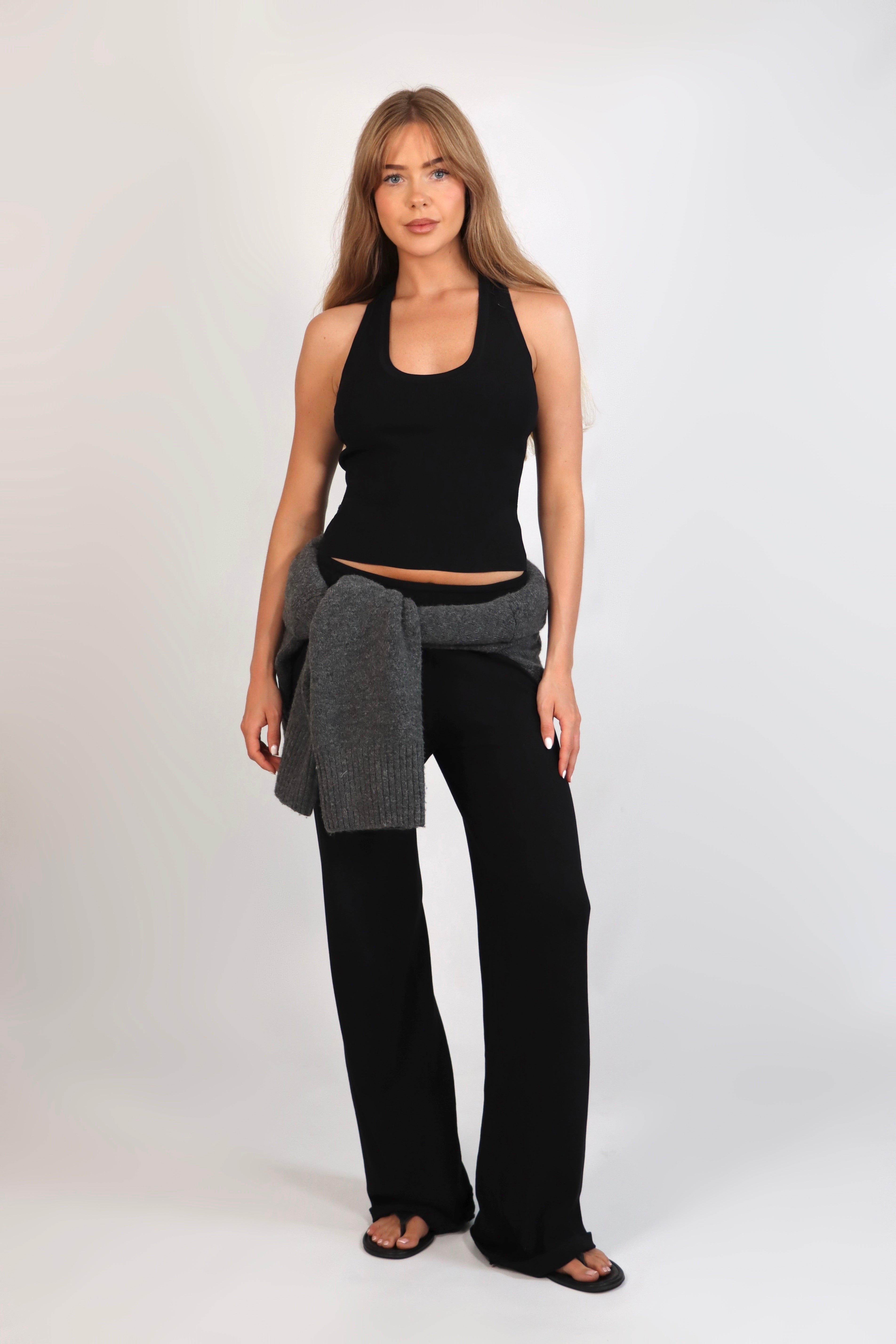A woman wearing the Freya Tank, featuring a deep scoop neckline and a fitted racerback silhouette. The image highlights the fine rib fabrication and the body-skimming fit of the top in a neutral setting.