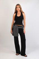 A woman wearing the Freya Tank, featuring a deep scoop neckline and a fitted racerback silhouette. The image highlights the fine rib fabrication and the body-skimming fit of the top in a neutral setting.