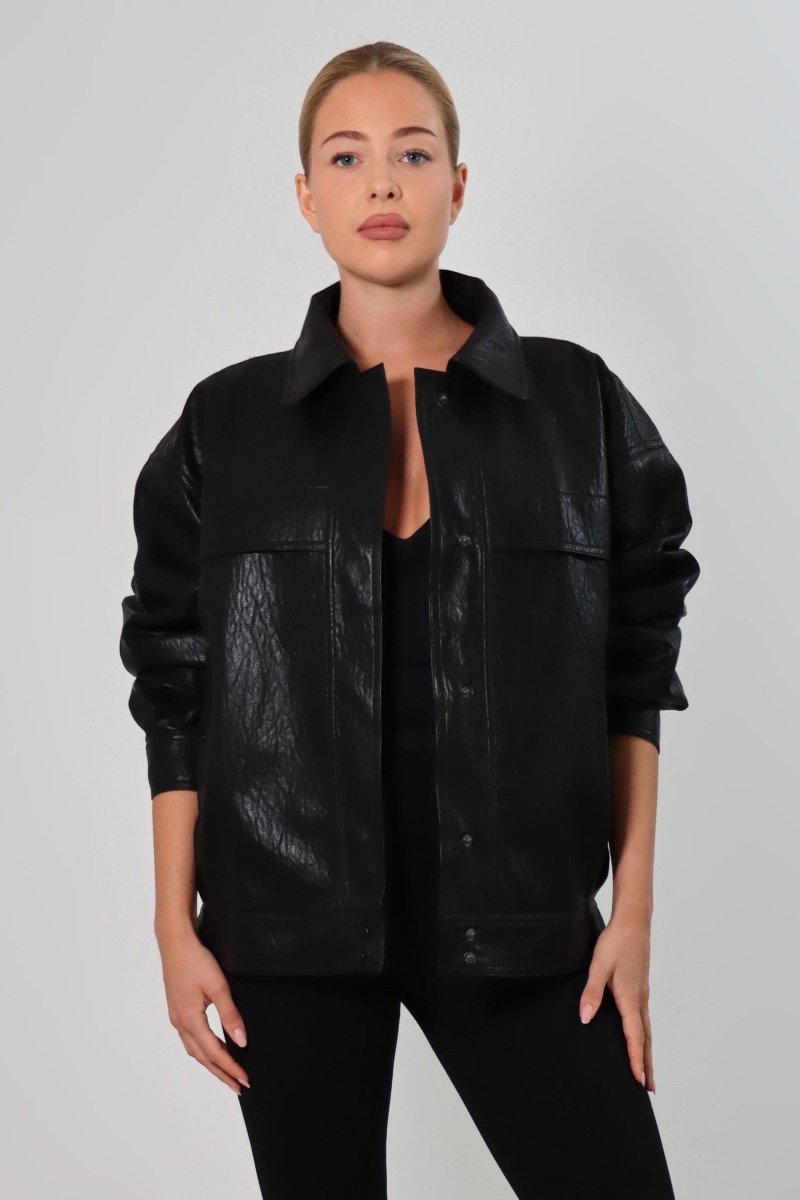 Model wearing a black textured leather oversized jacket with a structured collar and long sleeves, styled with black pants against a neutral background.
