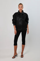 Model wearing a black textured leather oversized jacket with a structured collar and long sleeves, styled with black pants against a neutral background.
