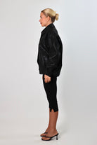 Model wearing a black textured leather oversized jacket with a structured collar and long sleeves, styled with black pants against a neutral background.
