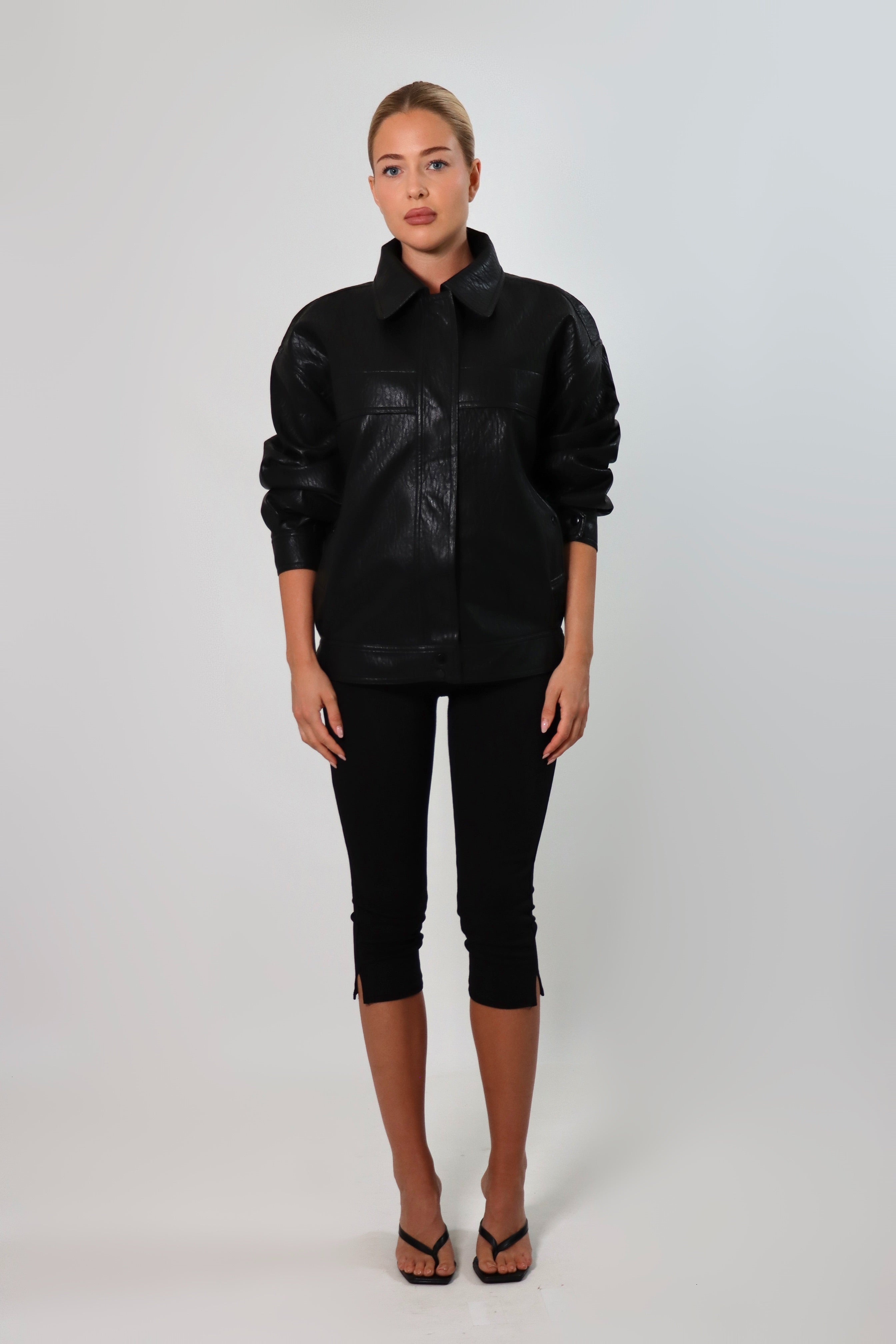 Model wearing a black textured leather oversized jacket with a structured collar and long sleeves, styled with black pants against a neutral background.
