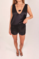 Woman wearing a black sleeveless satin top and satin shorts set on a white background from April Seven.