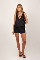Woman wearing a black sleeveless satin top and satin shorts set on a white background from April Seven.