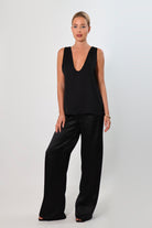 Black: Model wearing a black satin sleeveless top with a deep plunging neckline and matching satin pants for a sleek monochrome look.