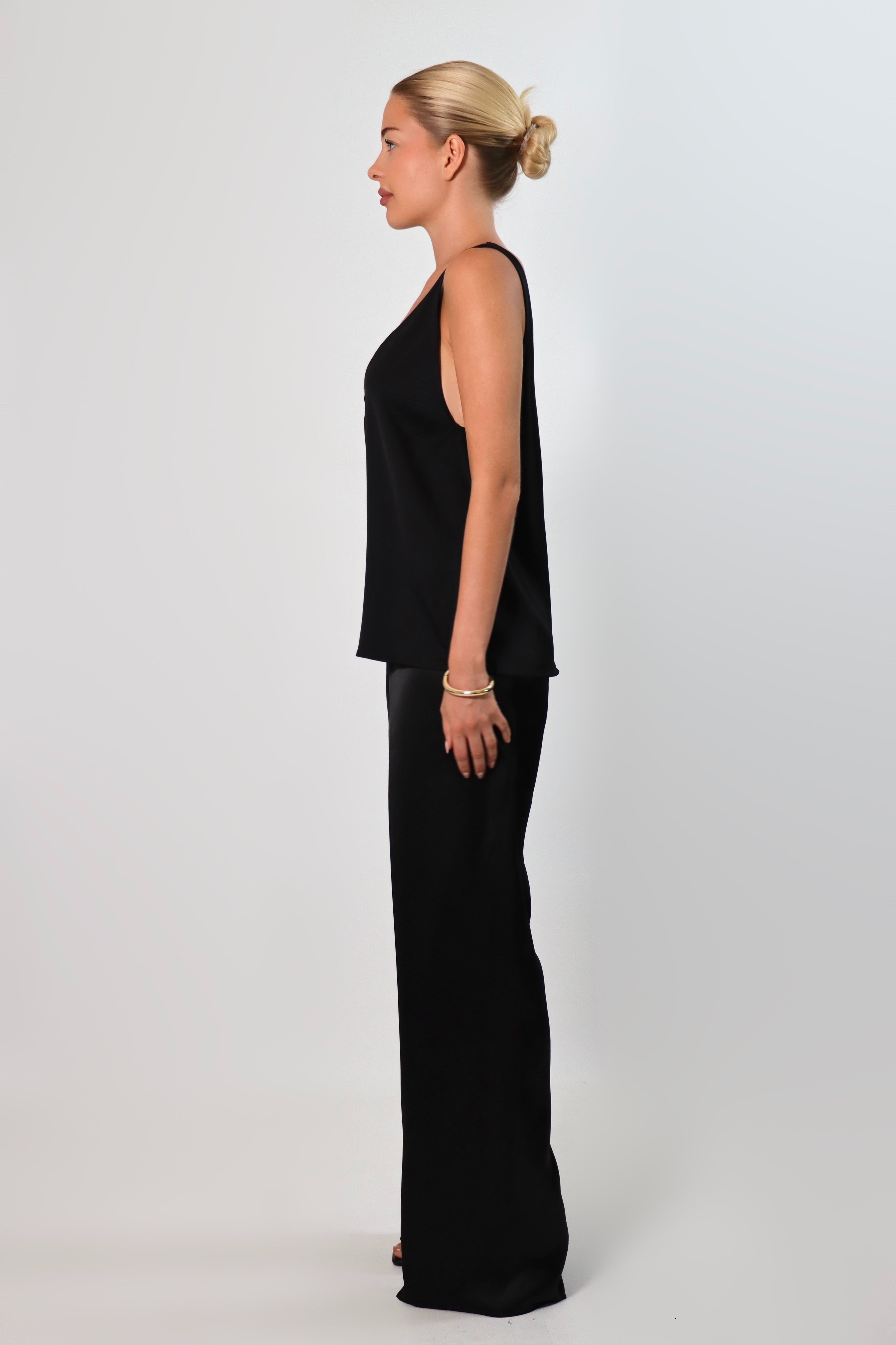 Black: Model wearing a black satin sleeveless top with a deep plunging neckline and matching satin pants for a sleek monochrome look.