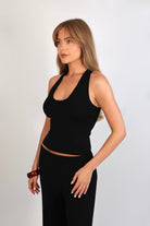 A woman wearing the Freya Tank, featuring a deep scoop neckline and a fitted racerback silhouette. The image highlights the fine rib fabrication and the body-skimming fit of the top in a neutral setting.