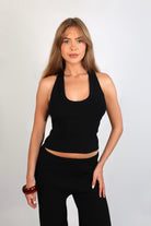 A woman wearing the Freya Tank, featuring a deep scoop neckline and a fitted racerback silhouette. The image highlights the fine rib fabrication and the body-skimming fit of the top in a neutral setting.
