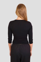 Woman wearing a black 3/4-sleeve top with V neckline and black pants against a plain background