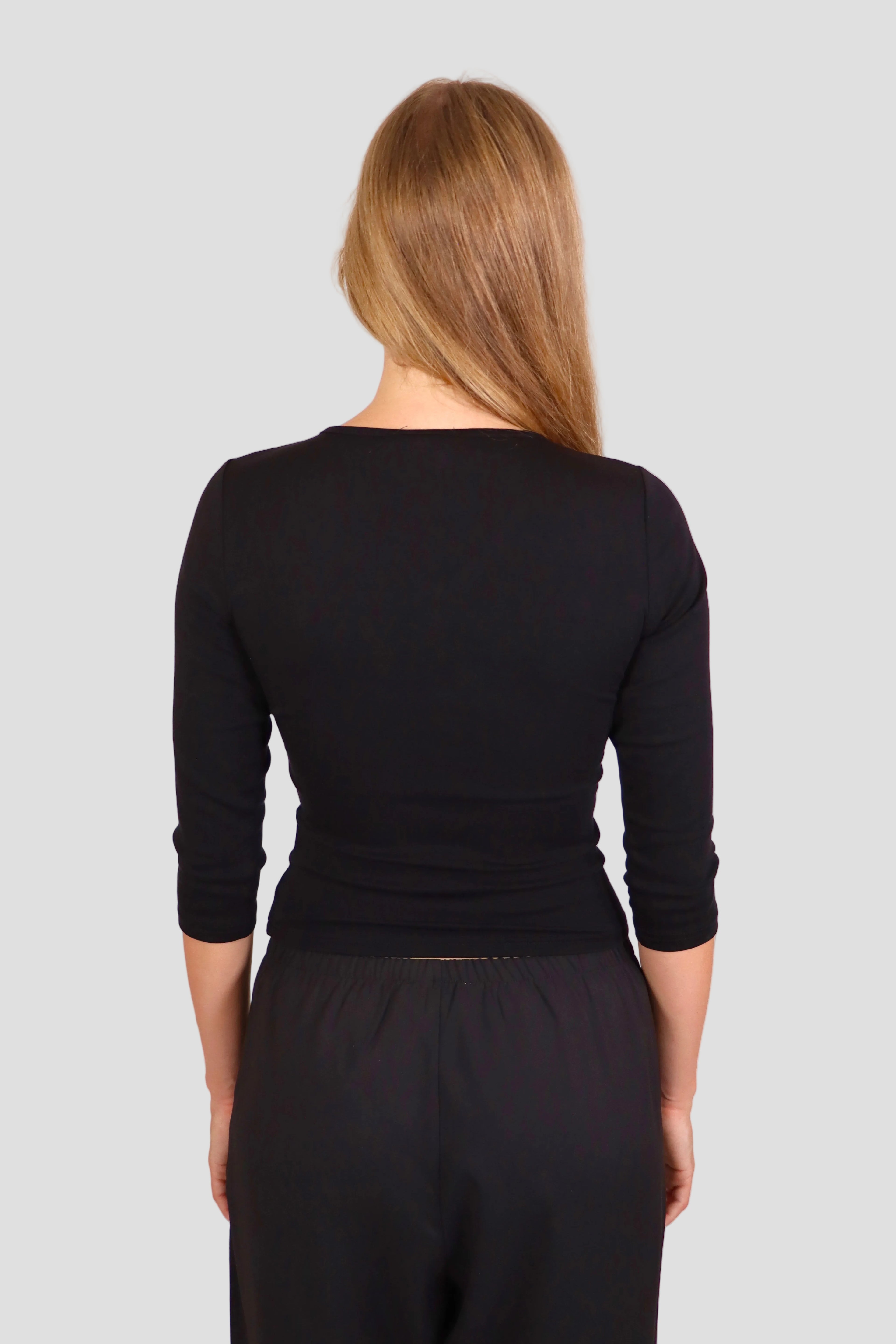 Woman wearing a black 3/4-sleeve top with V neckline and black pants against a plain background