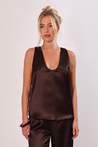 Model wearing a brown satin sleeveless top with a deep plunging neckline and matching satin pants for a sleek monochrome look.